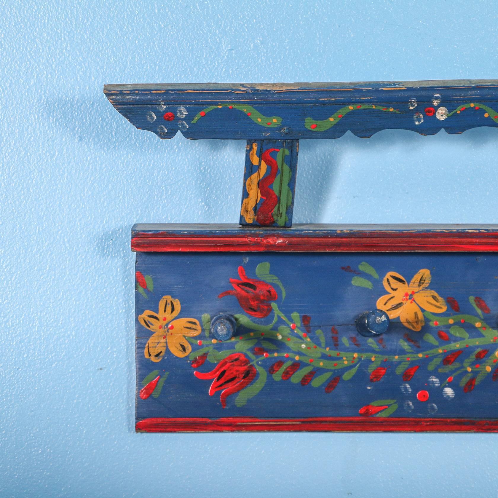This long 8.5' hanging wall rack still maintains its vibrant blue and red paint, with folk art flowers strewn along the full length. The 17 wood pegs alternate between 5.25" and 4.75" long. The upper rack was originally used to display