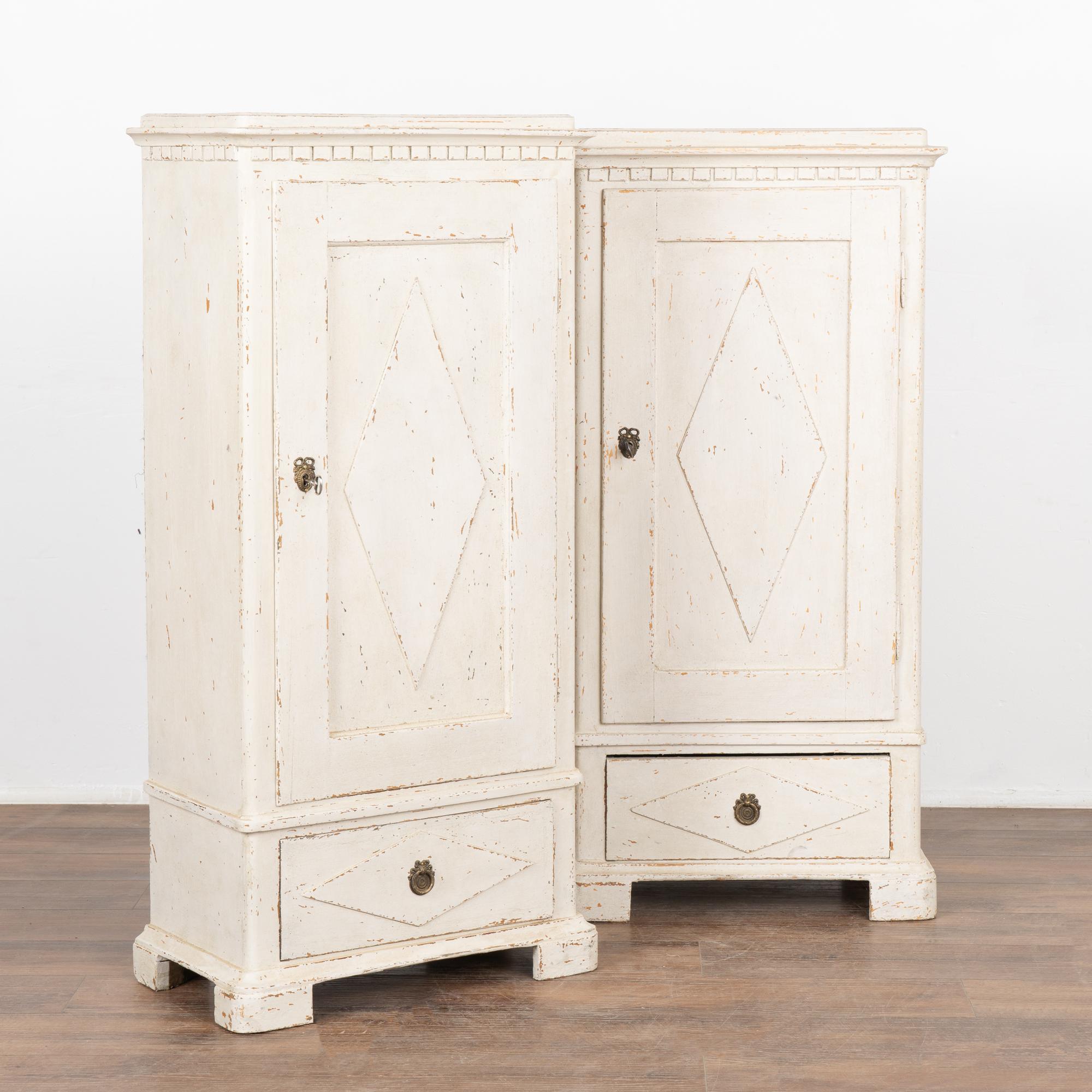 Pair, Gustavian narrow column pine cabinets with traditional diamond motif, dentil molding and lower drawer.
Newer, professionally applied white painted finish has been gently distressed fitting the age and grace of these cabinets.
Made of pine,