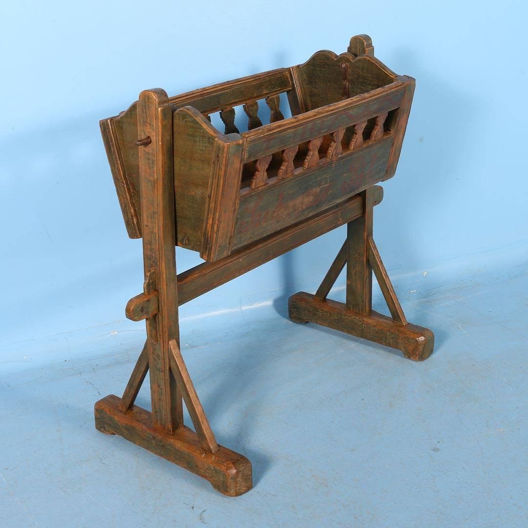 One can hear the whispers of soft lullabies and imagine a mother's hand gently rocking her baby in this delightful standing cradle. Where the original green paint has been worn away over the years, the natural pine comes through adding to the patina