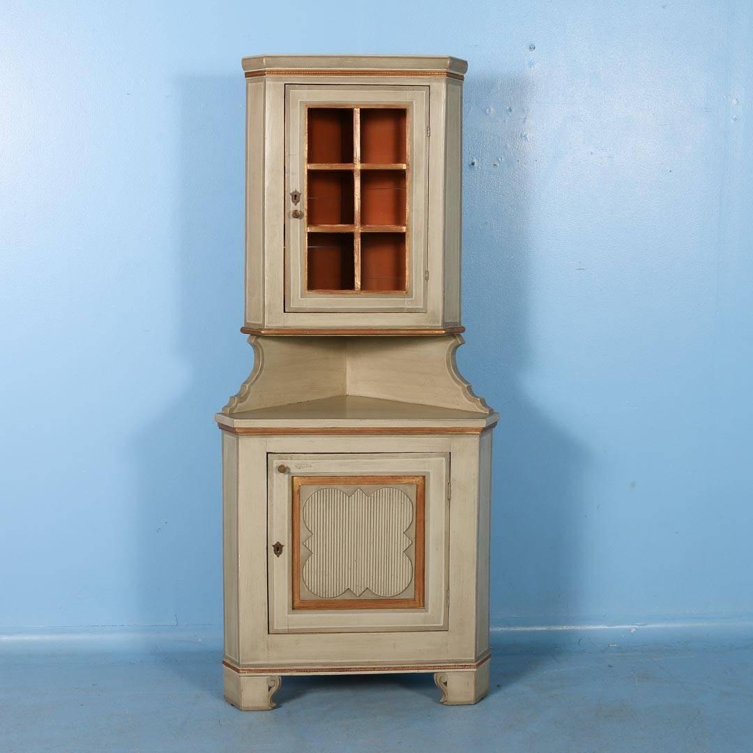 Late 19th century pine corner cabinet painted grey with gilded moulding. Made in two parts with a hinged glass door above and a cupboard door below, the inside is painted a salmon color. The corner cabinet was made in the 1880s, while it was painted