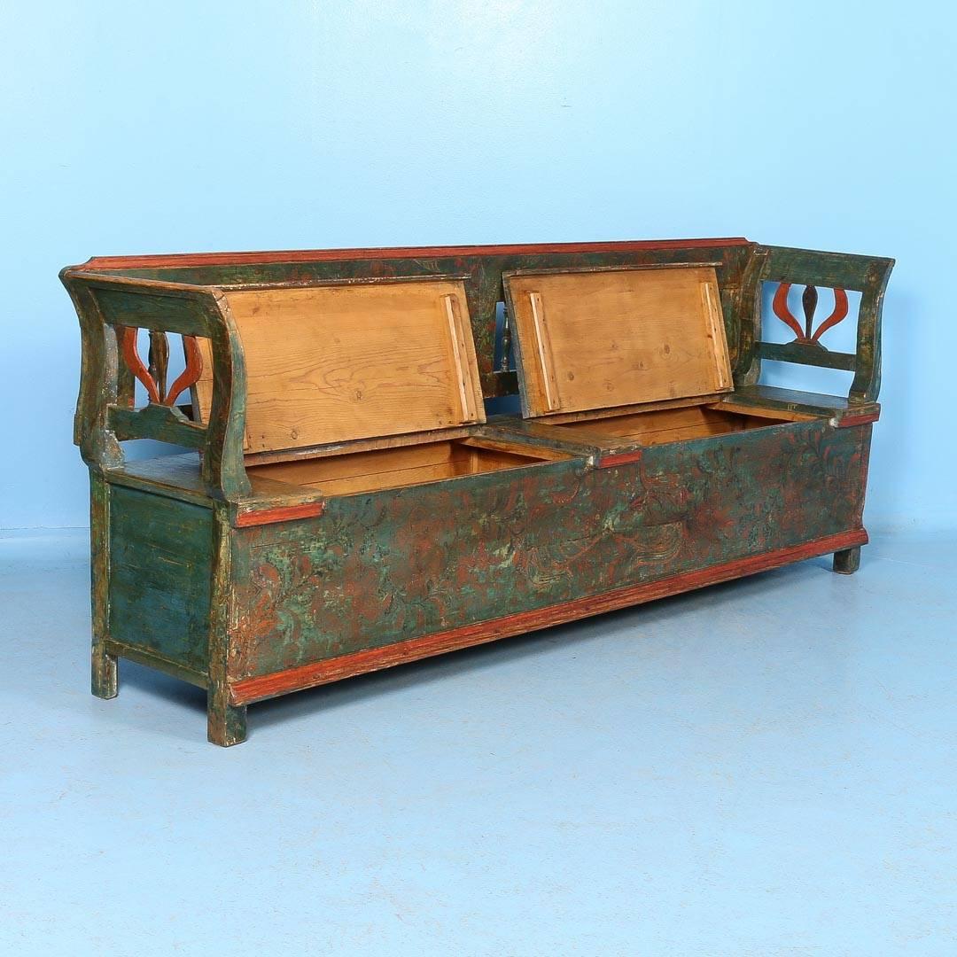 Antique Hungarian pine storage bench with original green and soft red/orange paint, circa 1860. The two seats are 19.5″ high and hinged with two separate storage areas inside. Over the green base color are flowers and vines in a dark rust and where