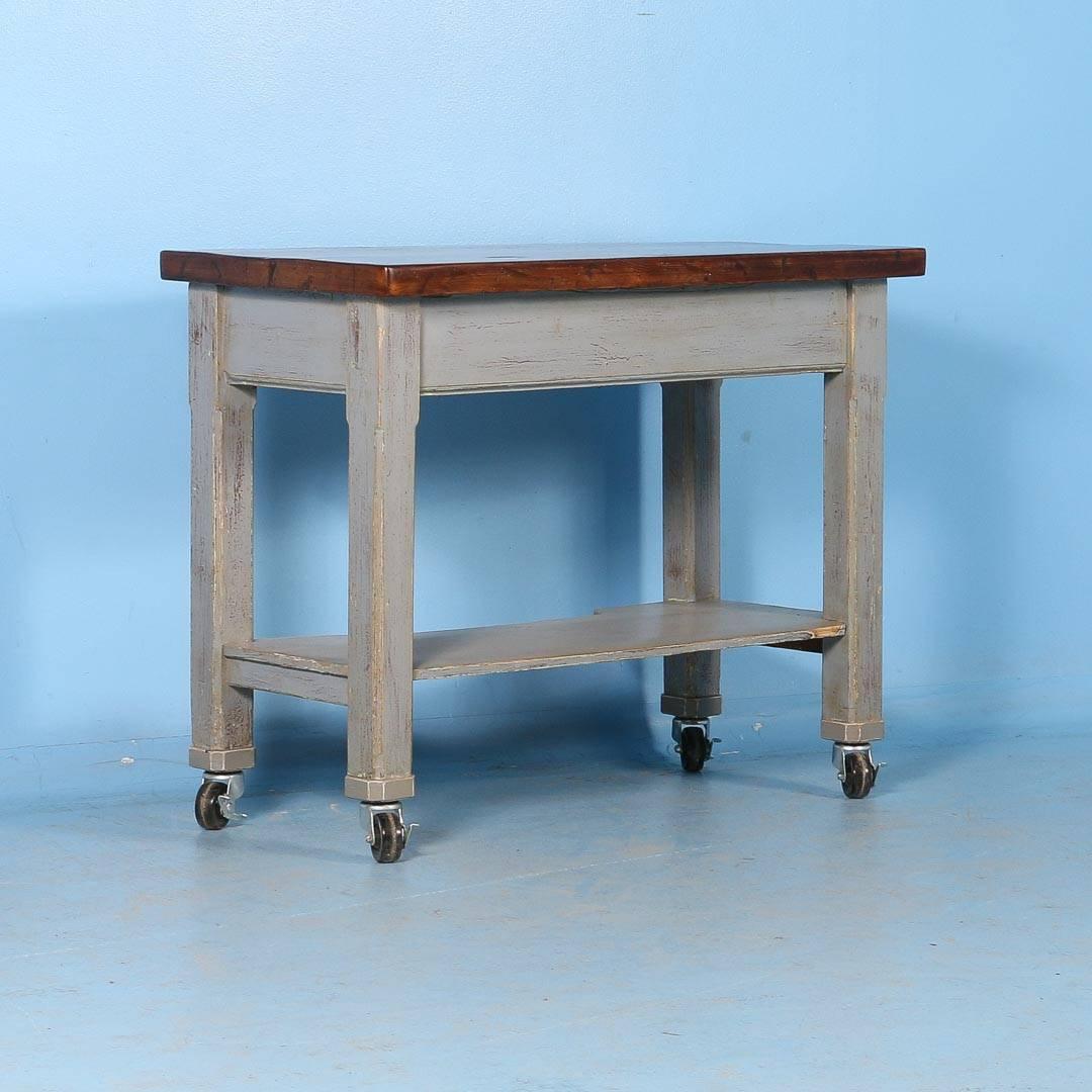 This kitchen island originally served as a work table. The base still maintains its original grey painted finish, the distressing adds to the character of the piece. The stained wood top create a great contrast to the painted base with three drawers