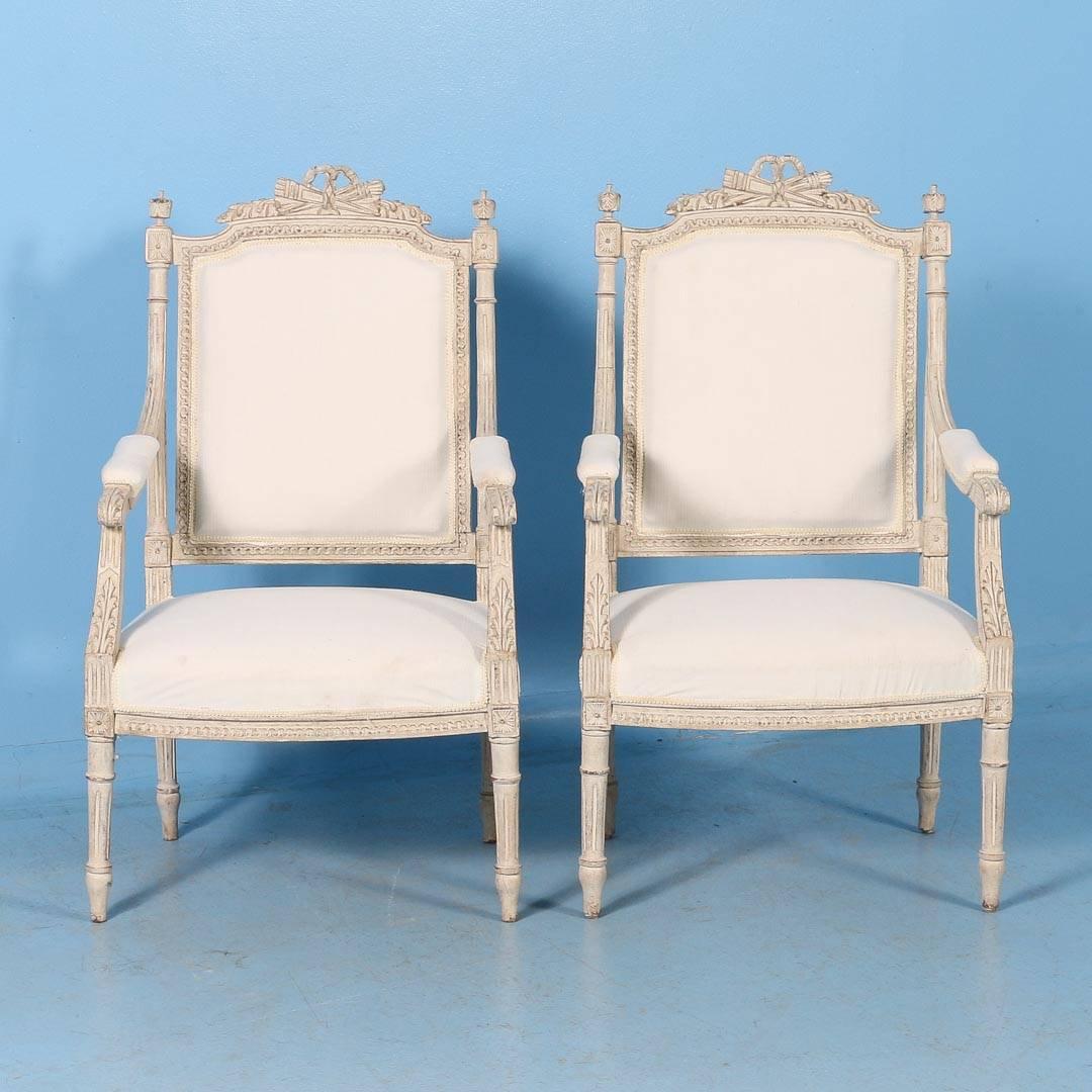 Graceful with a romantic air, this pair of Swedish Gustavian period armchairs still maintain their charming original white paint. Notice when looking closely the delicate carved details throughout every aspect of the chairs, including the arms,