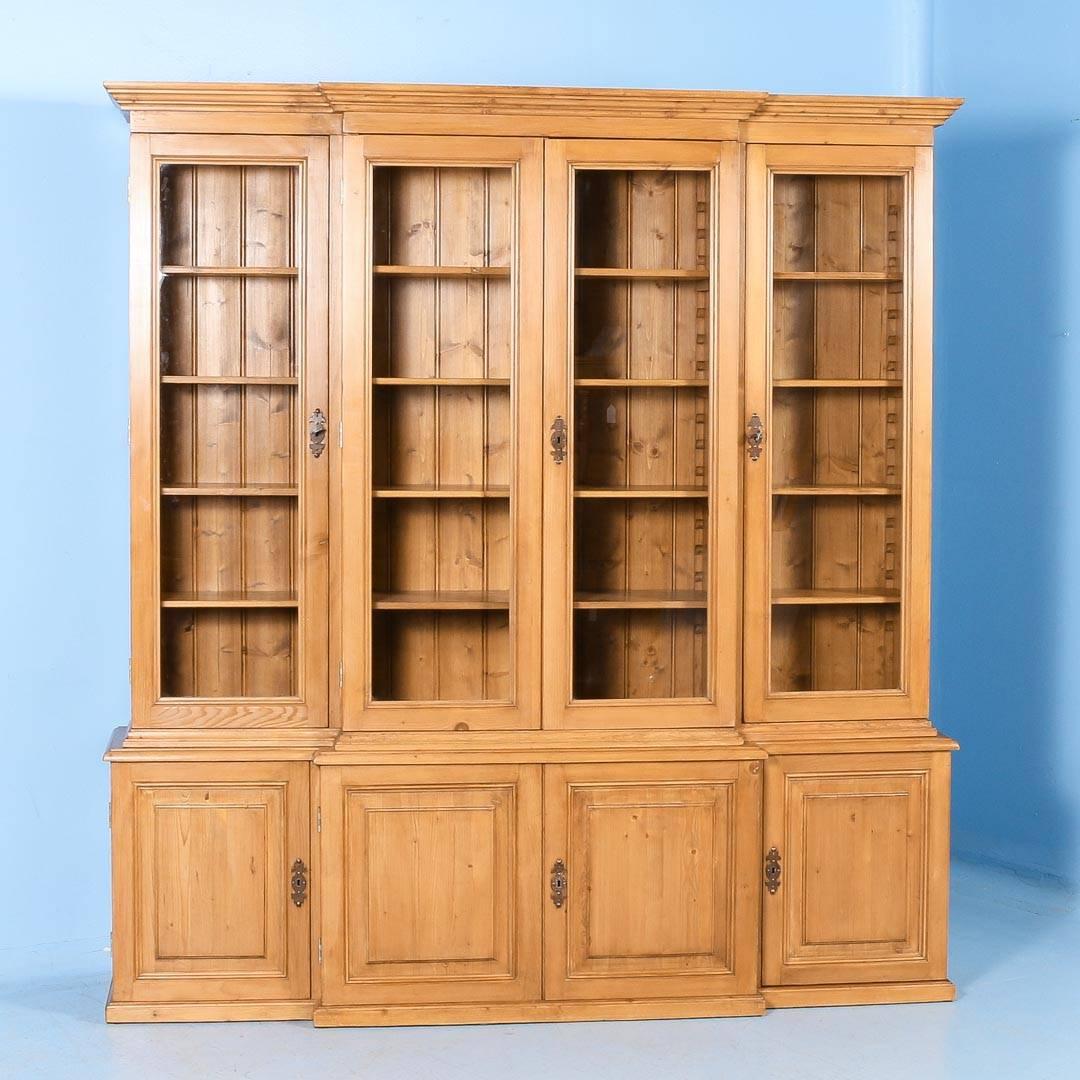 This large pine bookcase has four tall glass doors and adjustable shelves, allowing for ideal interior display options. The entire piece has been professionally restored; assuring that it is structurally strong and ready for placement and use. A wax