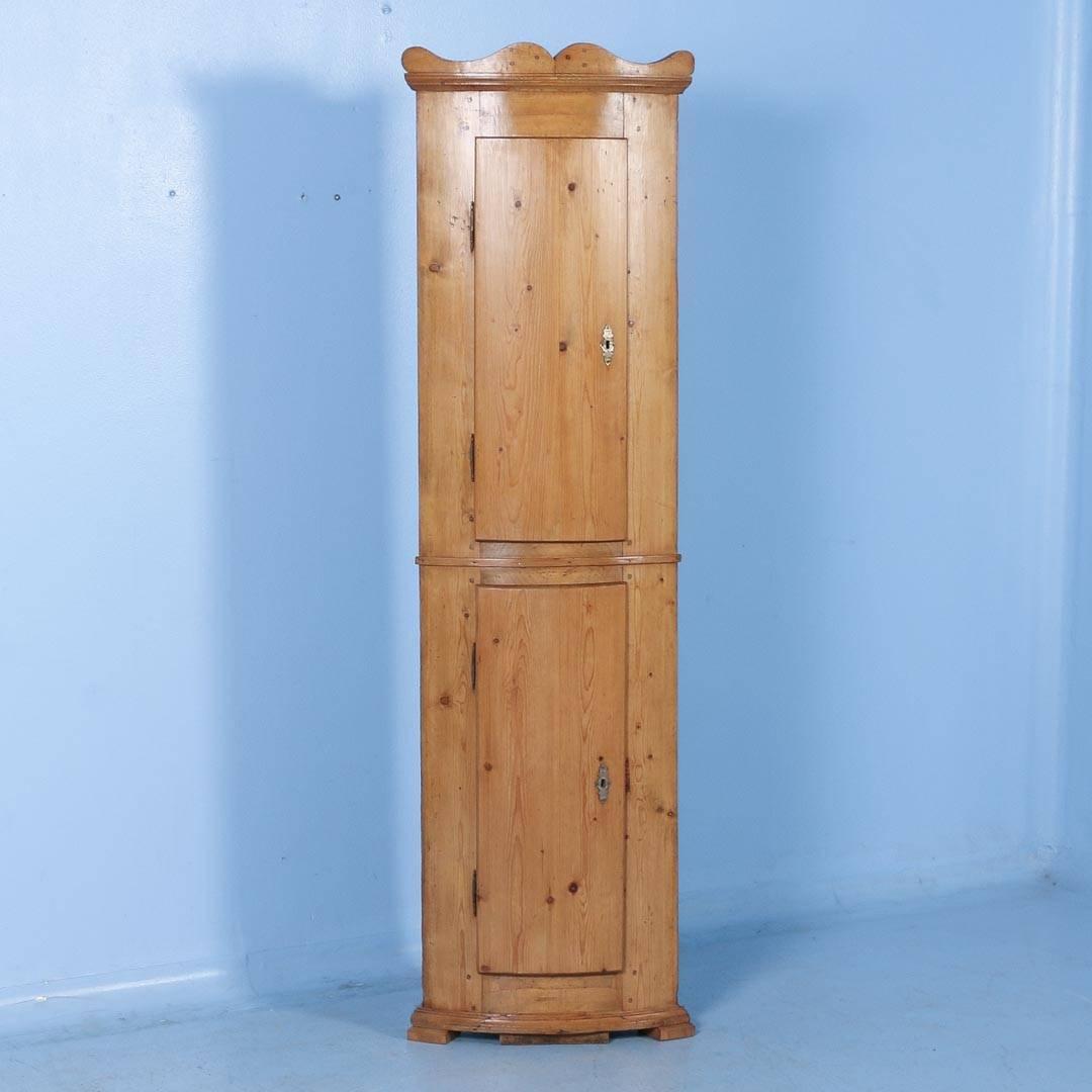 This is a unique and narrow corner cabinet with two curved doors which follow the elegant bowed front. This cabinet has been professionally restored and finished with a satin wax, bringing out the natural beauty of the warm pine. The top cabinet has