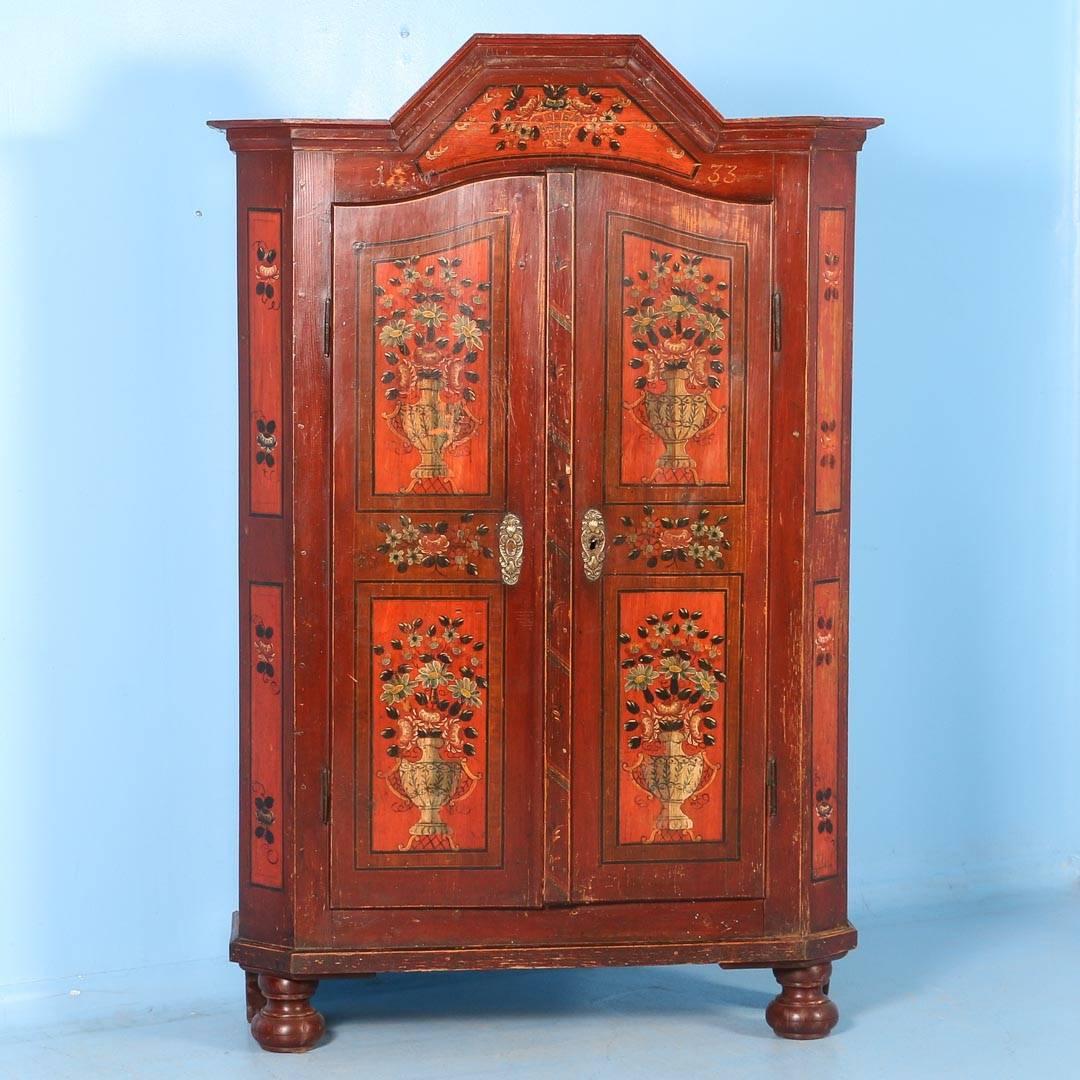 This two-door antique armoire from Hungary, still retains it’s original red paint and includes the date of 1833. There are floral details painted throughout the cabinet. Each of the four-door panels has a painted decorative handled vase filled with