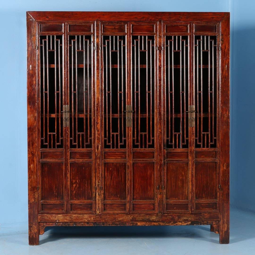 The elogated open panels are visually striking in this stunning cabinet from China.  The original red and wood-toned painted finish is slightly distressed, revealing the age and adding depth and character to the cabinet while the lacquered finish