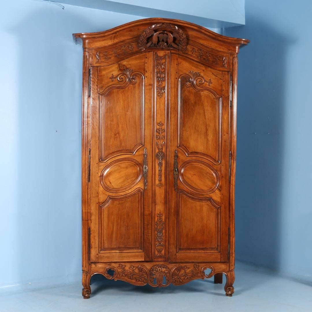 An 18th century wedding or bridal armoire from France, made of chestnut with a stunning deep, rich patina that reveals the beauty of age. Topped by a traditional curved crown above a hand-carved pair of love birds surrounded by oak leaves. Two doors