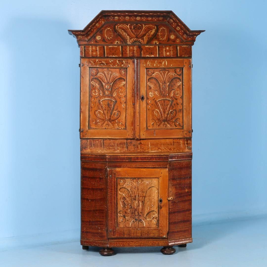 This beautiful Swedish Dalarna cupboard with original painted earth tone details, is full of character. There are two cupboard doors above with two shelves inside and a single door below. Painted just below the detailed crown molding is the date