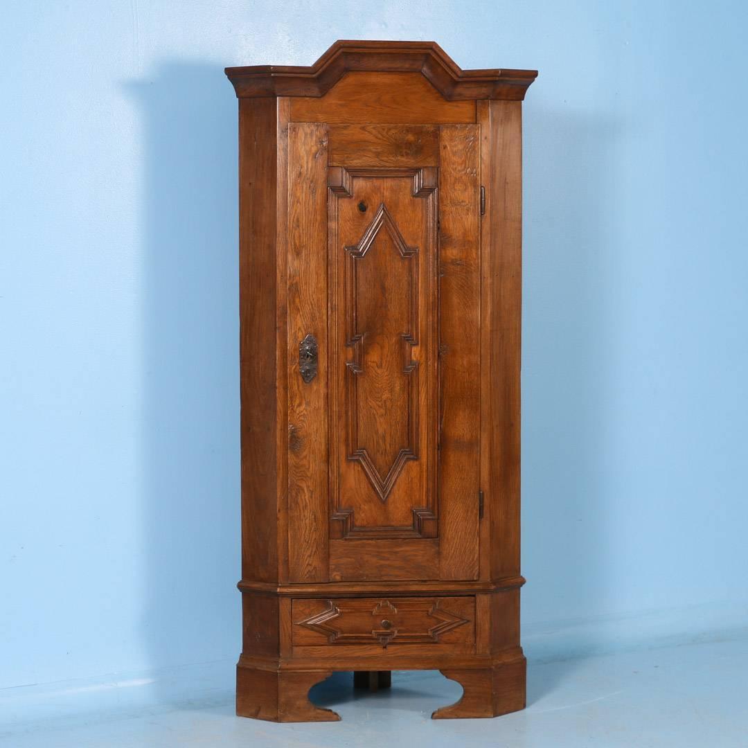 This antique single door oak corner cabinet stands just a few inches shy of 6 feet tall. Made in Denmark around 1860-1880, it has a fully functional bottom drawer, a single door with a raised panel, carved molding and comes with the original