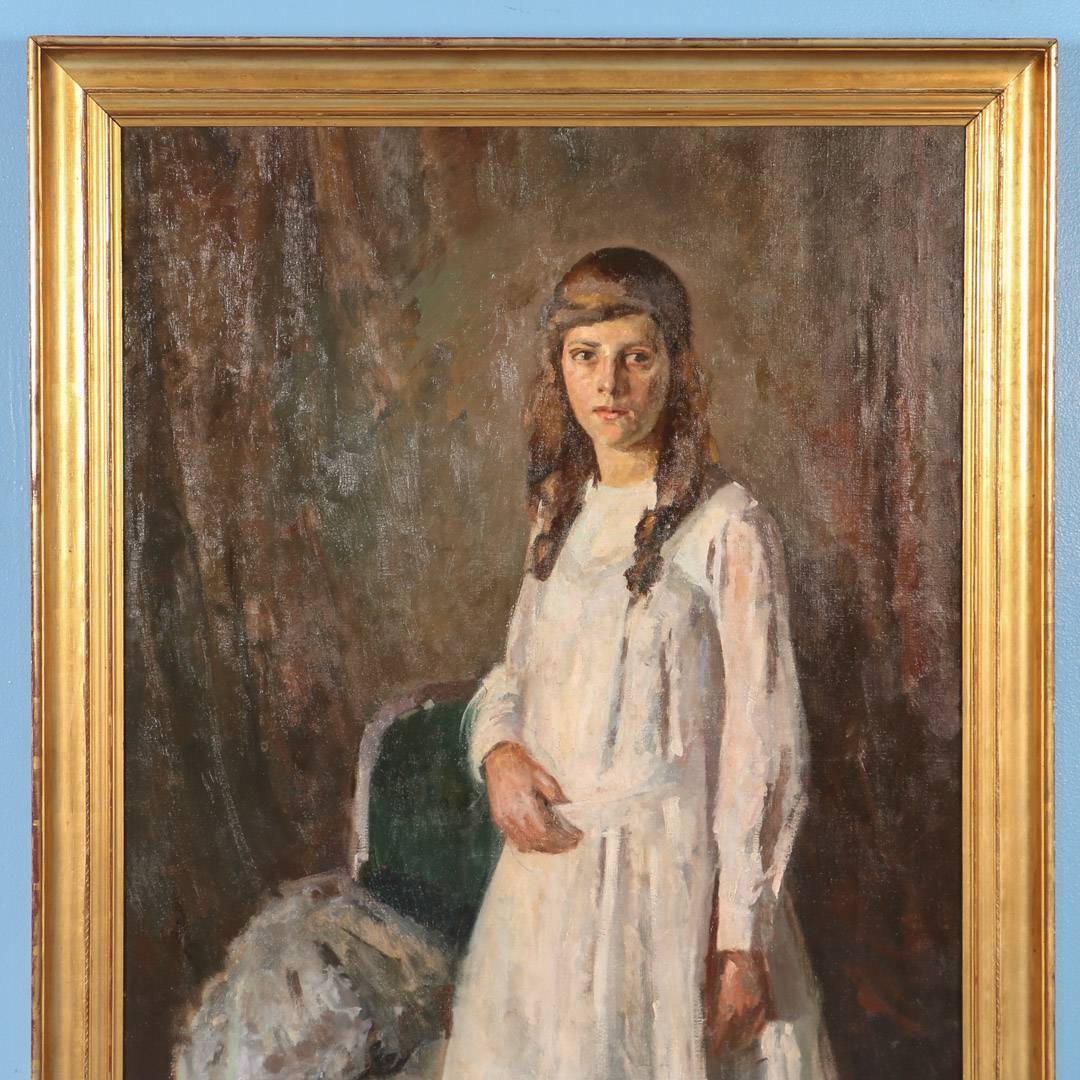 Large unsigned oil on canvas painting of a young girl with long brown hair, standing wearing an all-white dress, white shoes and stockings. Beside her is a chair, upon which appears to be a white fur cape. This painting is impressive in size and