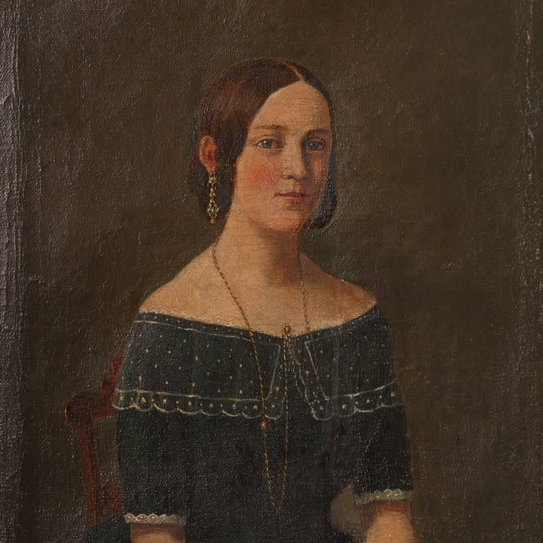 Small unsigned oil painting of a young Danish woman seated with hands crossed on her lap, circa 1840-1860. Mounted in a giltwood frame, there is a companion painting, of an older woman that is the same size in the same frame. Please take a moment to