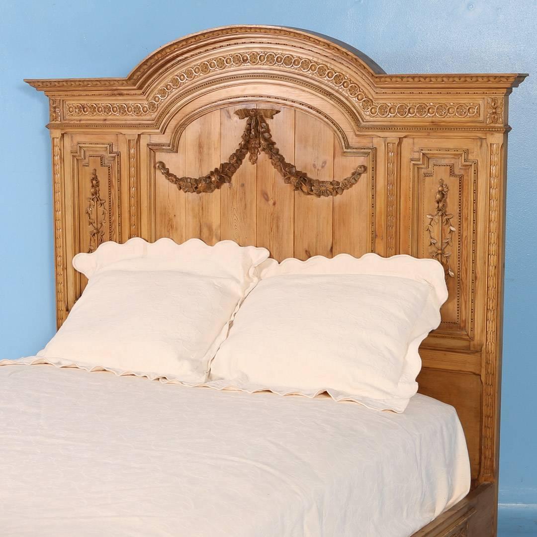 Exceptional antique pine queen size bed from France, circa 1860-1870. The headboard features heavily carved crown moldings and side panels with large swags of carved flowers accenting the headboard and footboard. Notice how the wide band of carved