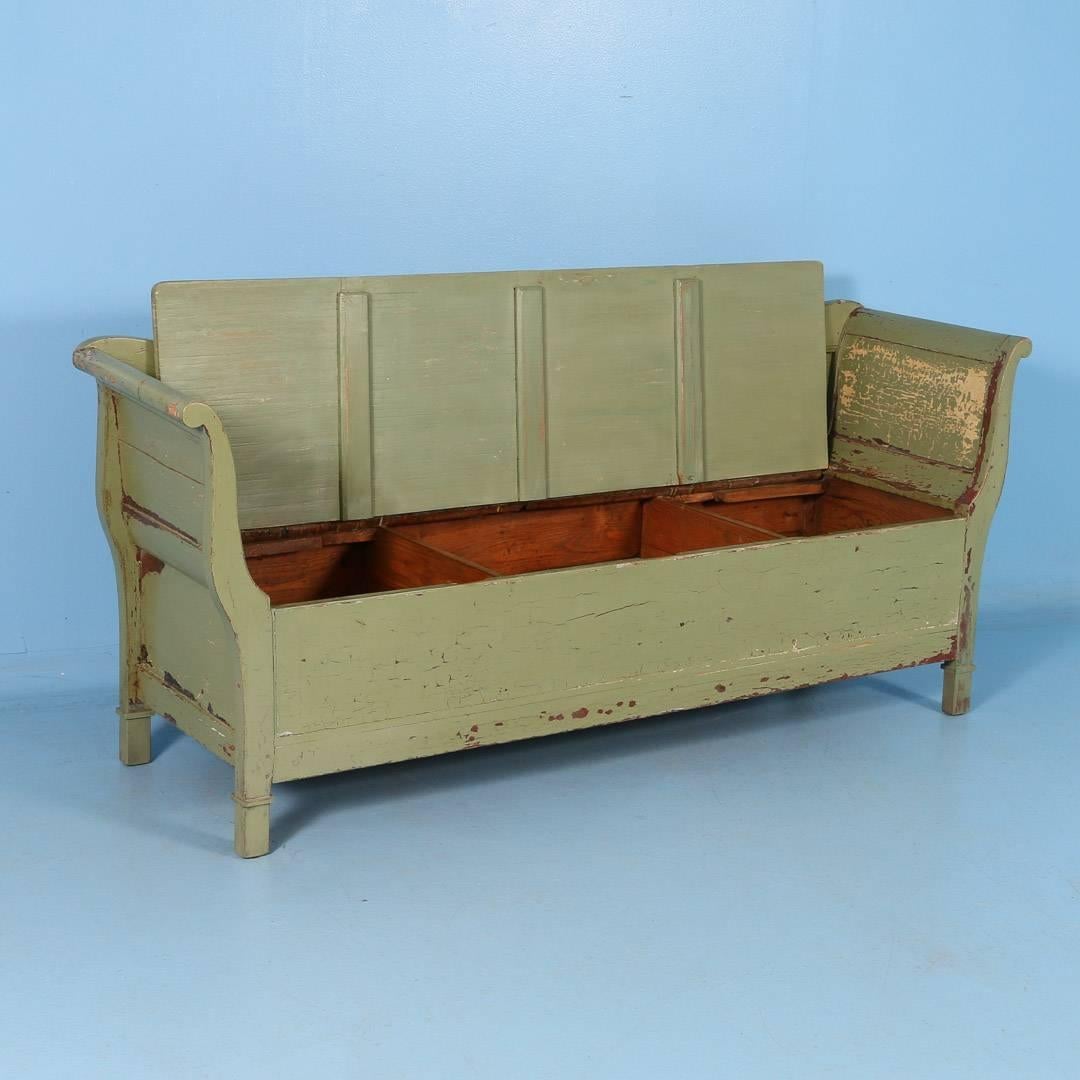 Antique Swedish painted storage bench, circa 1860. The seat of this pine bench is hinged with ample storage inside. The green paint is worn in places exposing an undercoat of light butter cream colored paint. A great country piece with lots of
