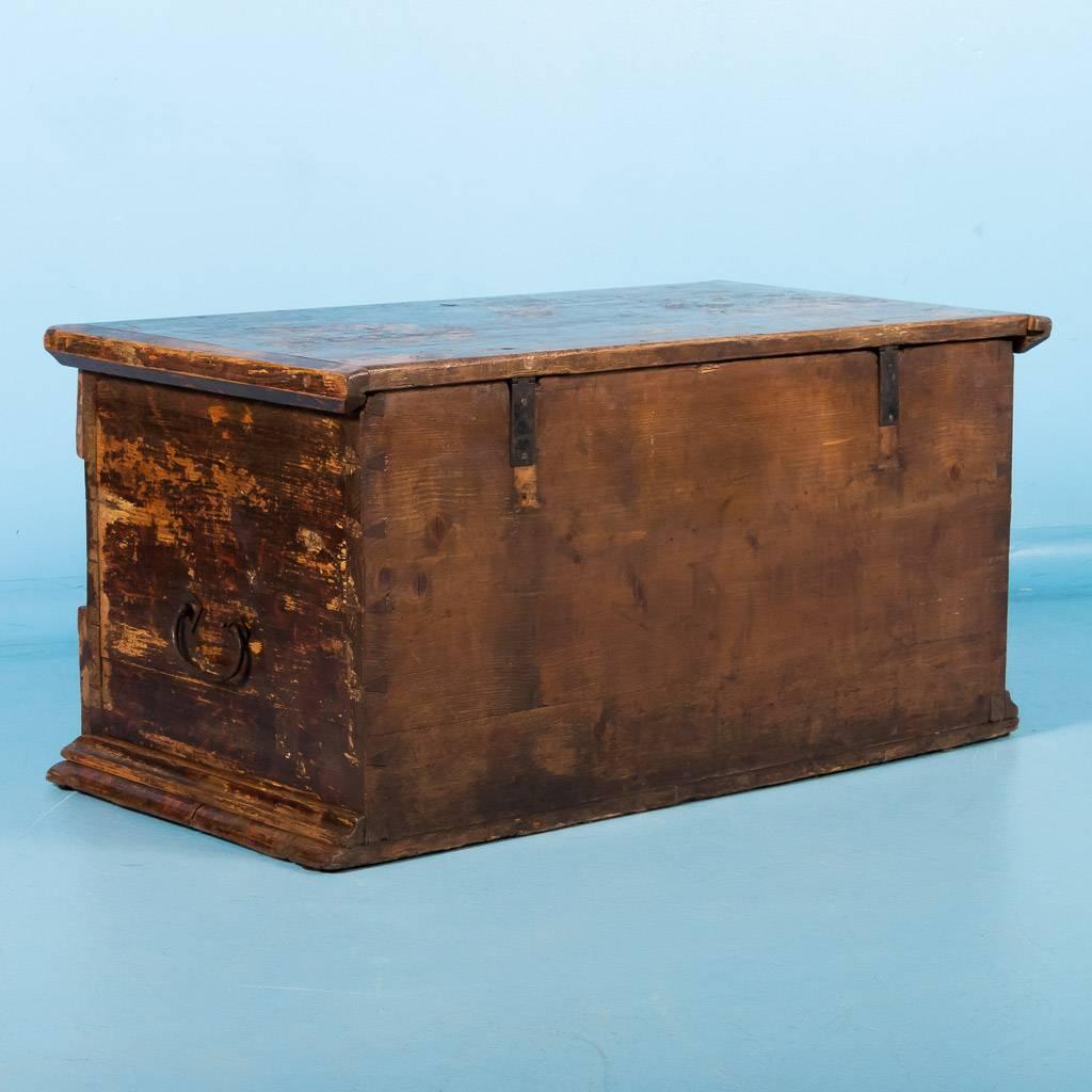 This original painted brown trunk from Hungary has a traditional Folk Art flower pattern that includes colors of red and yellow. The false drawer below is flanked by a half column detail and inside the top is a small utility box, that when opened,