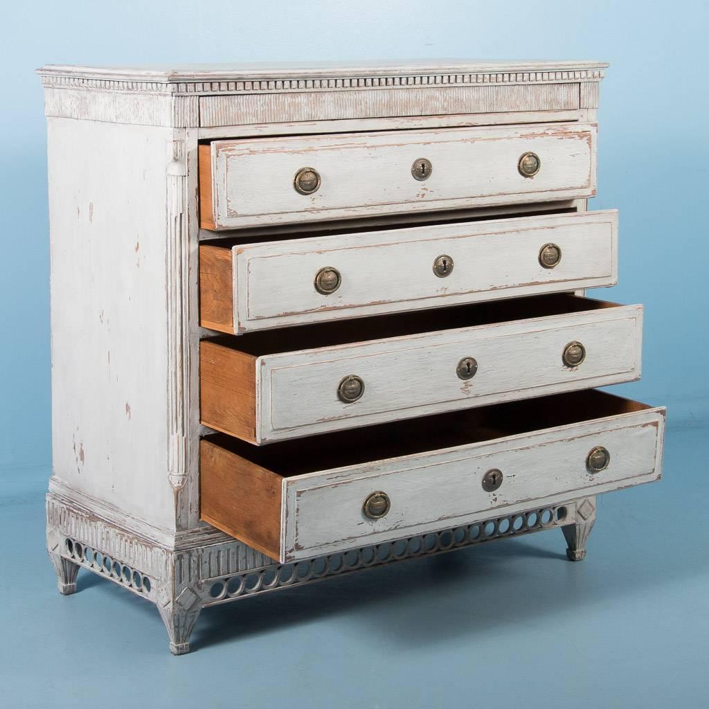 Gustavian Style antique oak chest of drawers from Sweden, circa 1820-1840. Made in two parts, the upper case with four drawers, rest on a base with pierced carving and short tapered feet. The lightly worn gray paint over oak, brings out the carved