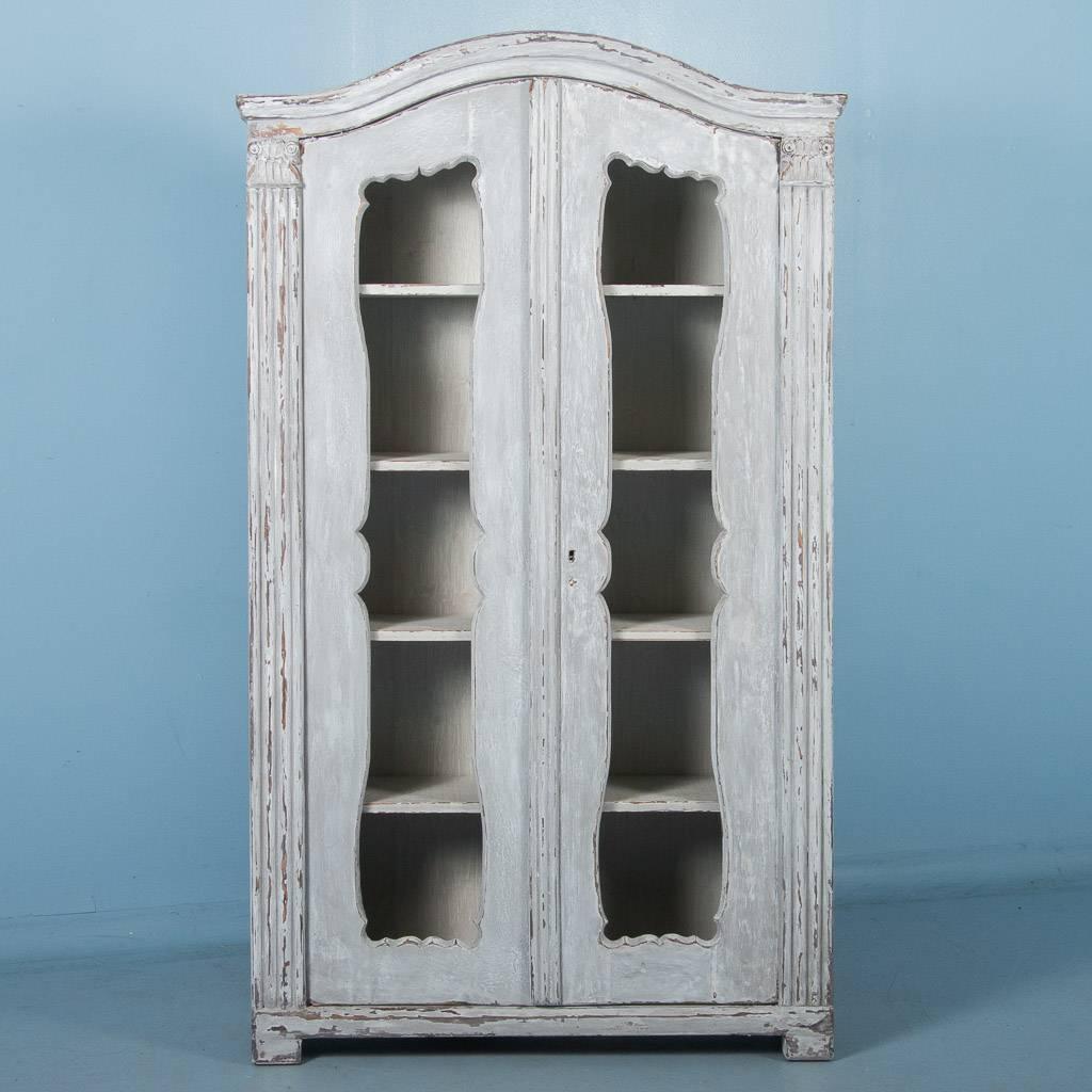 Antique 19th century Swedish pine two-door bookcase, circa 1850. The arched doors are without glass giving the bookcase a more open and accessible feel. Where the blue gray paint has been scraped there are hints of natural pine showing through