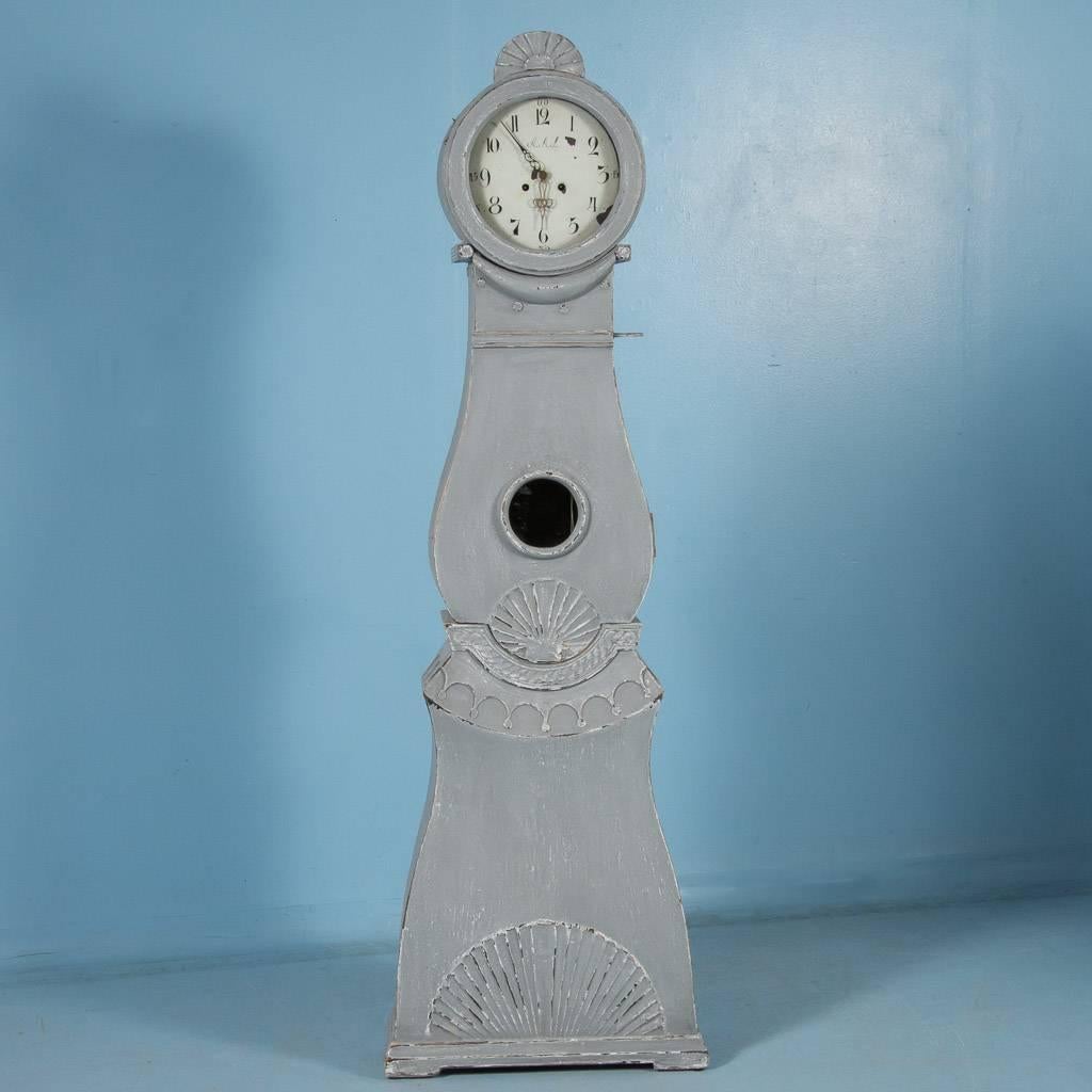 Graceful curves and unique carving accentuate this striking antique grandfather clock from Sweden. The carvings here represent the Gustavian Period, circa 1830. Please examine the close up photos to appreciate the distressed blue/gray painted finish