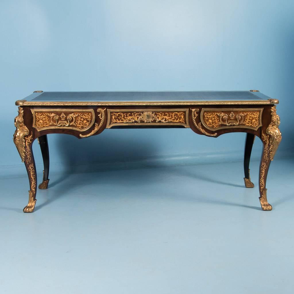 This French writing desk or ‘bureau plat’ in the Louis XV style, is finished with ornate brass ormalu mounts and a hand tooled leather top. The desk is freestanding which allows one to appreciate the intricate wood inlay and brass details on all