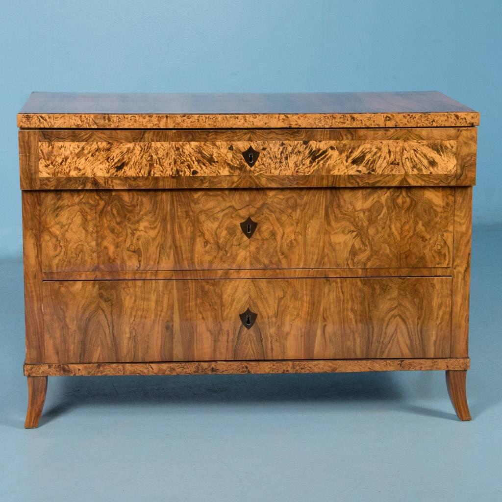 Antique Biedermeier chest of drawers from Germany, circa 1830. Each of the three-drawer fronts features book matched burl veneer with dark inlaid key escutcheons. Notice how the top drawer is accented by a light band of birch and how it steps out