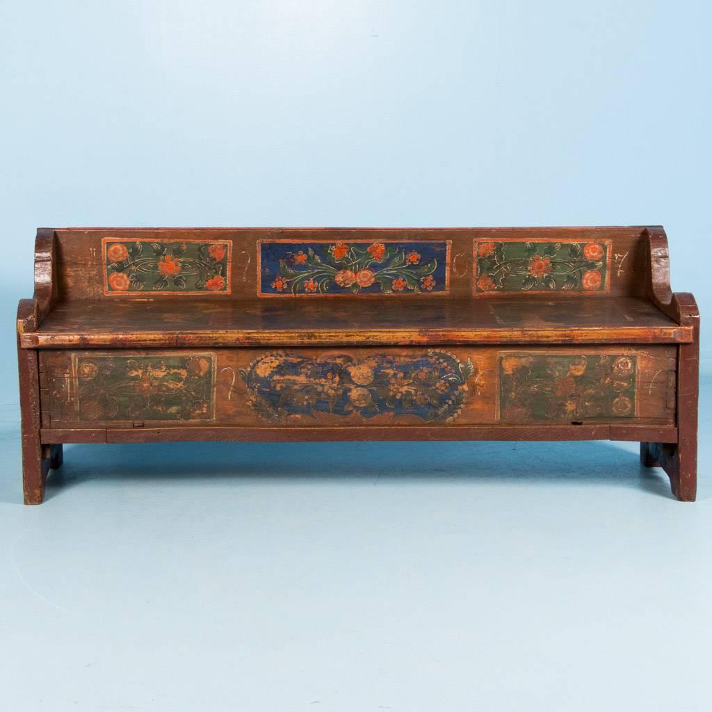 Antique storage bench from Hungary with original Folk Art paint, dated 1907. This sturdy pine bench is painted with an original rust colored background and three floral panels in green and orange on the back, seat and front. If you look closely, the