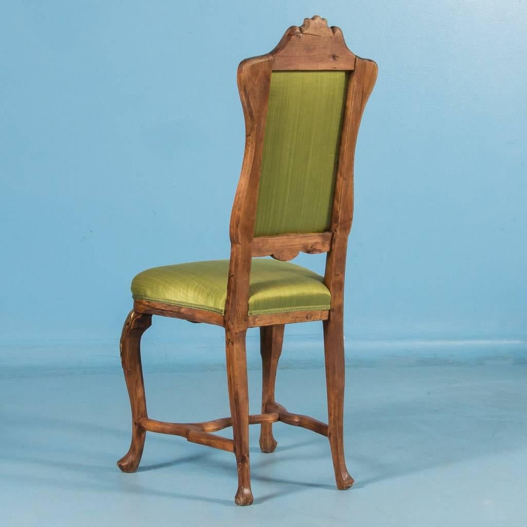 Set of eight carved antique upholstered dining chairs from Norway, circa 1850-1870. The high backs and seats are upholstered and covered in a green satin fabric which complements the dark natural hardwood of the frame. The four cabriole legs with