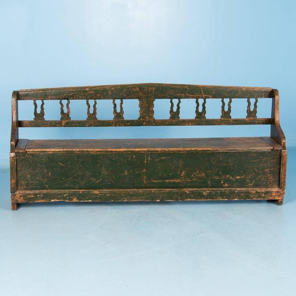 This antique Hungarian country pine bench, circa 1860, retains much of it's original green paint. This bench is perfect for a hallway or mudroom because of the shallow seat which lifts to access the storage compartment inside. Please take a moment