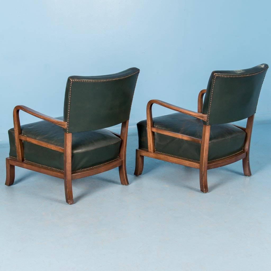 Pair of vintage Danish green leather armchairs, circa 1960 with a walnut stained hardwood frame. The original leather seat is slightly worn but in remarkable condition with a firm seat cushion that springs back. These are very comfortable arm chairs