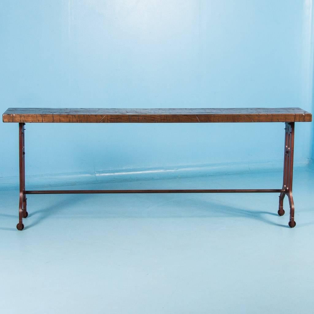 Made in the USA from reclaimed railroad box car flooring, this long oak console table features cast iron legs that come from old turn of the century machinery. The rustic top has a durable finish and the addition of an iron stretcher makes this