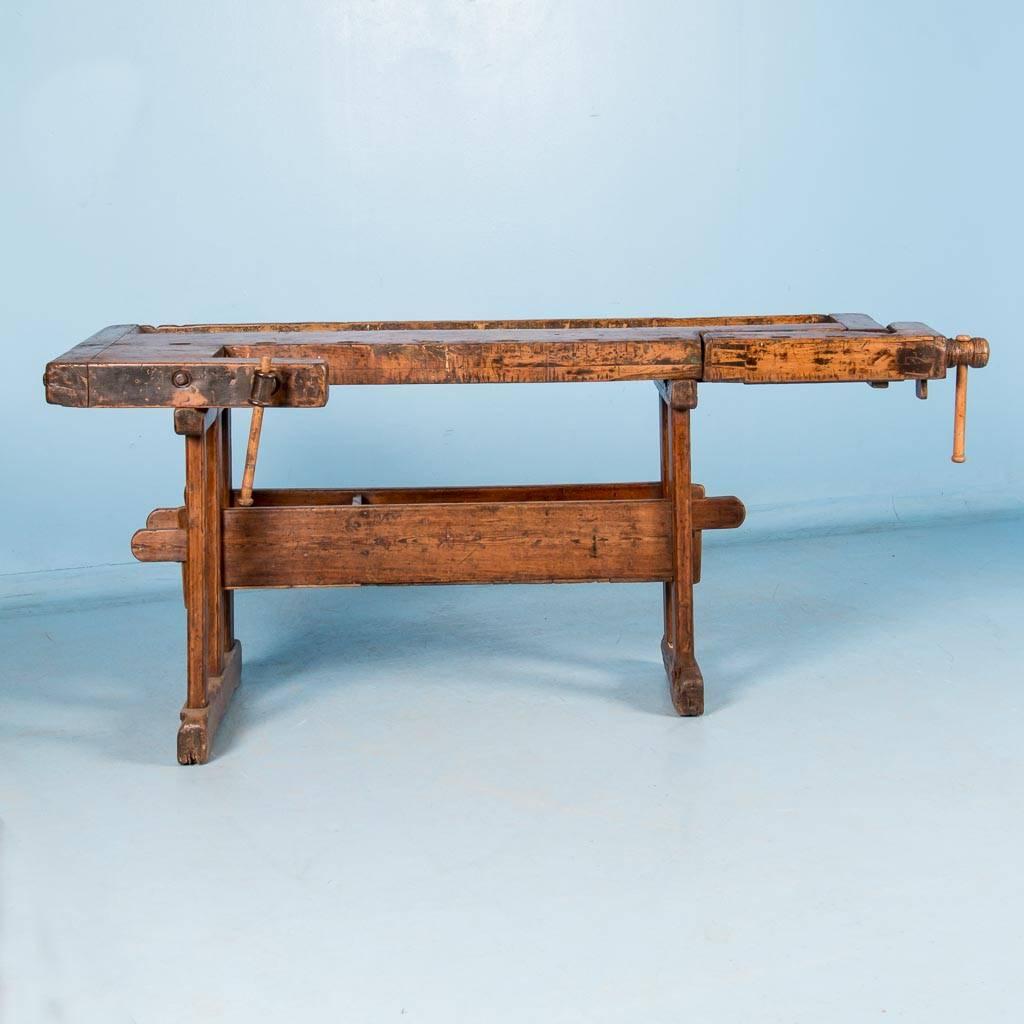 This circa 1900 antique hardwood workbench has a pair of vices with a wood handle and a recessed tray where the carpenter would lay his tools and for catching debris. The traditional keyed trestle base allows it to be assembled and taken apart or