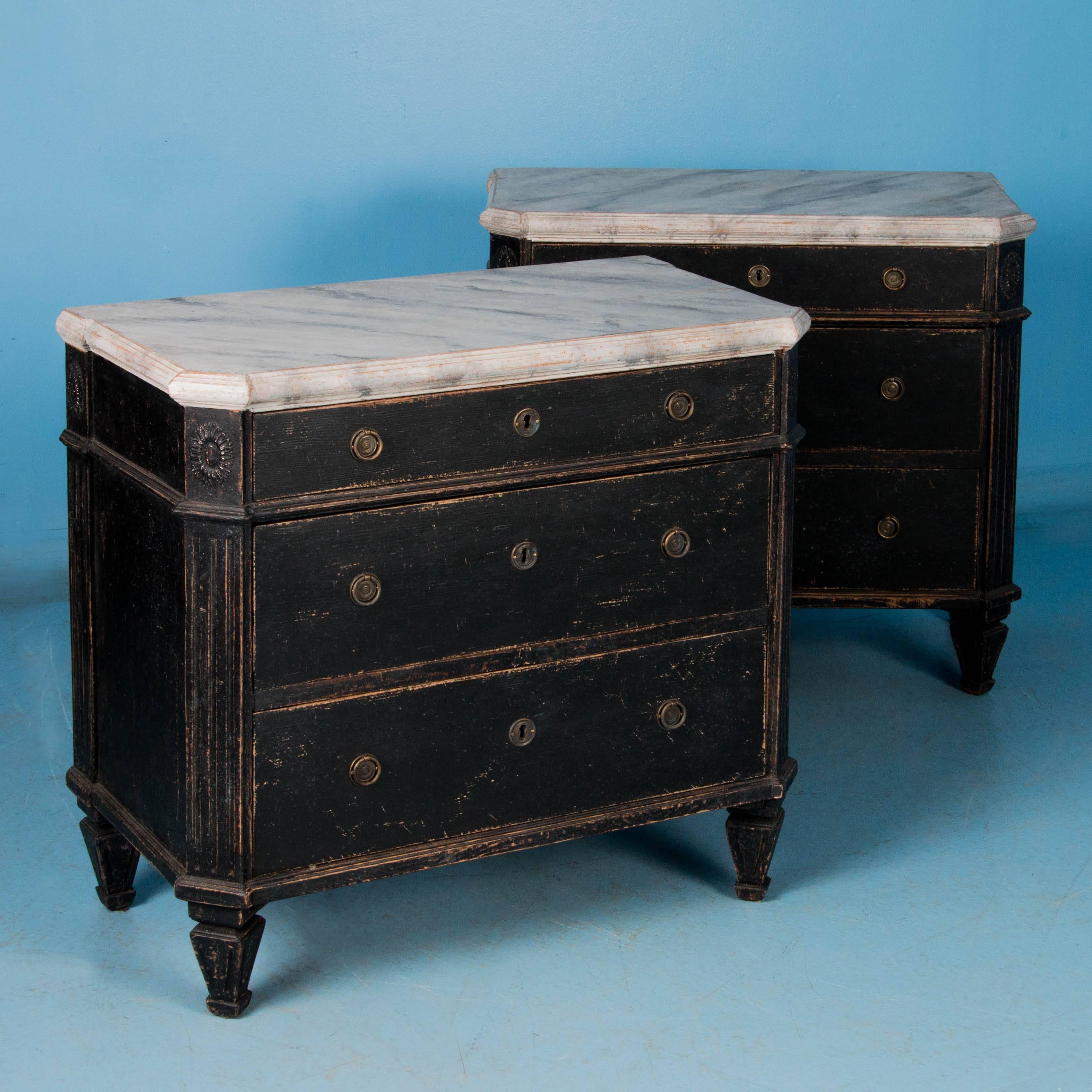 This pair of small antique chest of drawers, circa 1860, features painted white faux marble tops which are the perfect contrast to the black painted cases. The paint is lightly distressed allowing the natural pine to show through. Please take a