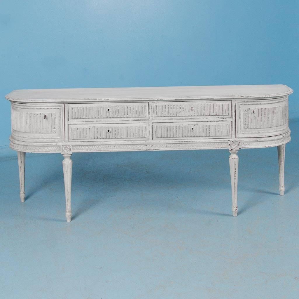 Elegant antique sideboard from Sweden, circa 1920, in the Gustavian Style with four drawers and two curved doors. The dark wood of the cabinet creates a nice contrast where the light gray paint has been slightly scraped. This sideboard may also be