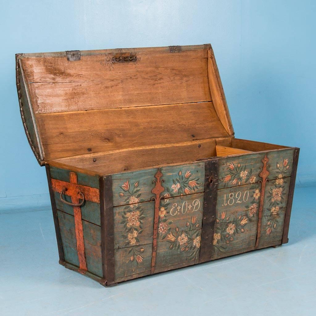 Antique dome top trunk from Sweden, dated 1820, with original pale blue painted background and laurels of white and rust colored flowers decorating the front. The black hand-wrought metal straps and hardware are all original. Please take a moment to
