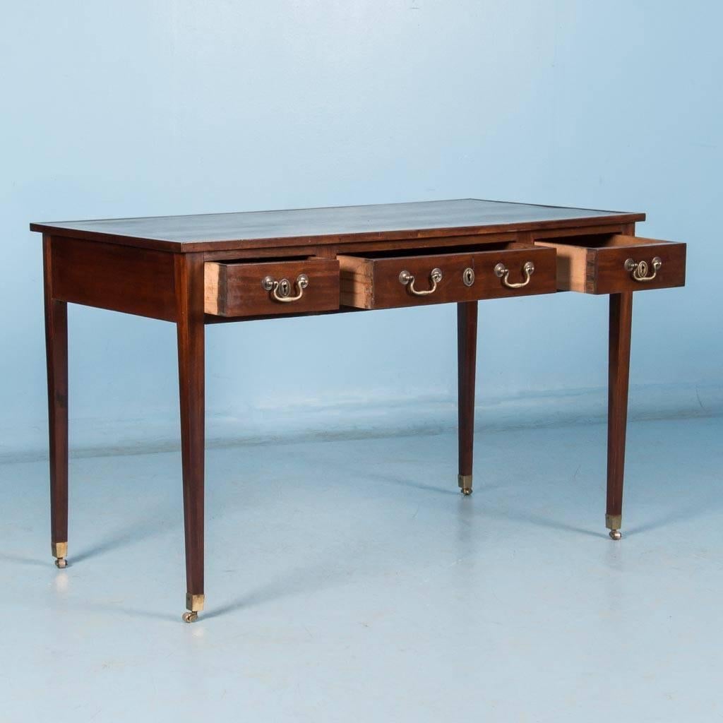 Antique mahogany desk from England, circa 1920 with a hand tooled gold border on a green leather top. The desk features three working drawers on one side and three imitation drawers on the other. Brass hardware is original and tapered legs rest on