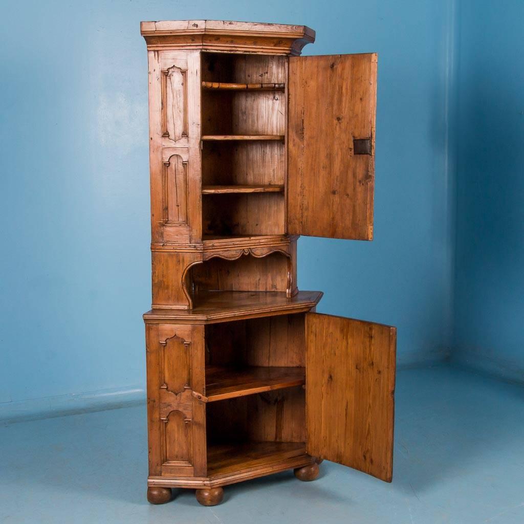 Antique pine corner cabinet from Sweden, circa 1820-1840, made in two sections with carved moldings on the upper and lower doors. The wax finish on this country pine cabinet enhances wonderful caramel color and patina of the natural pine. Please