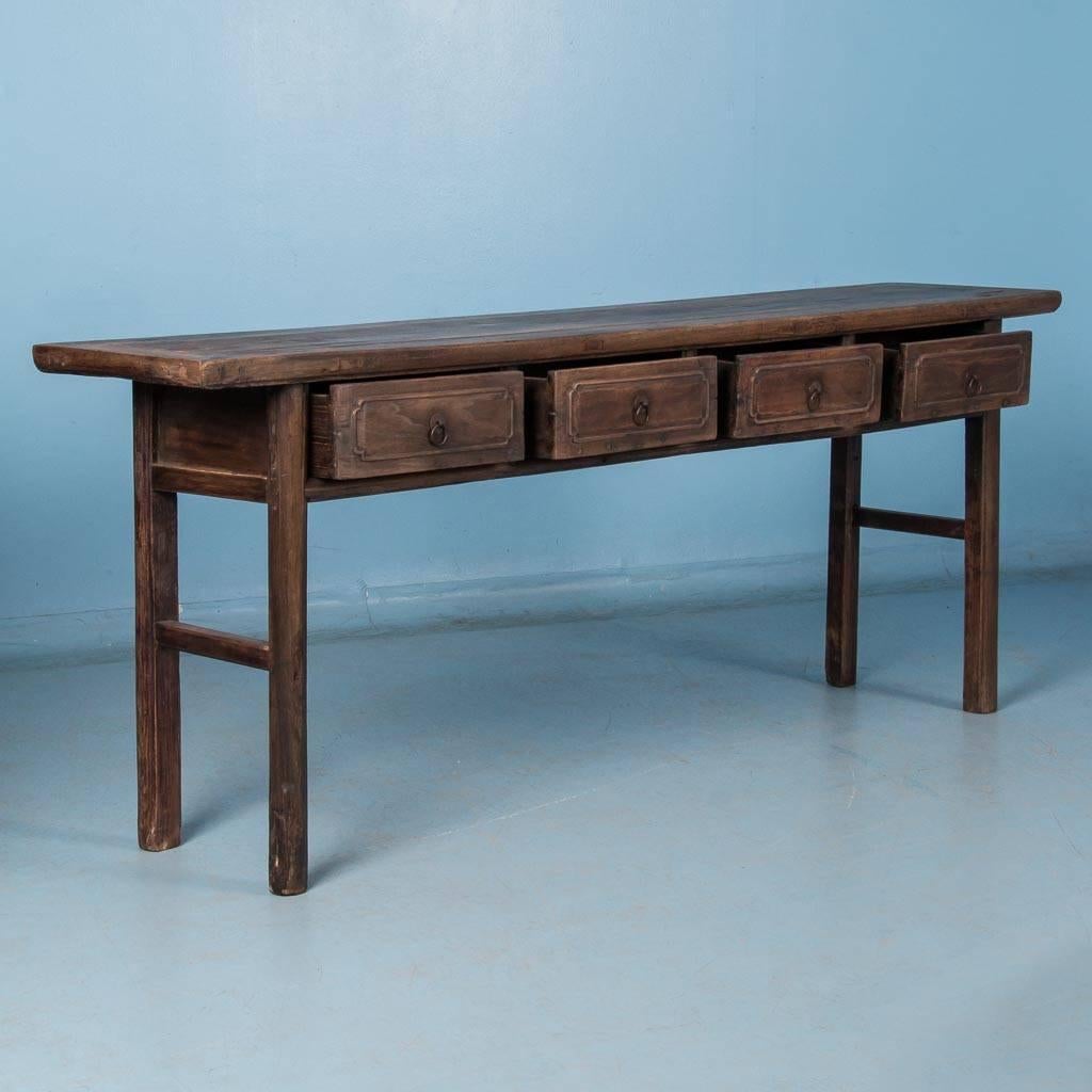 This circa 1840 console table is made of elm and features four drawers with brass ring pulls and is supported by elongated legs. The table's simple and clean lines give a country feel and would make a great server or buffet. Please take a moment to