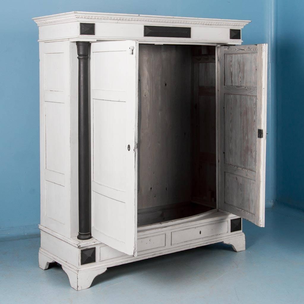 Impressive and statuesque, this country Biedermeier pine armoire is painted white with black accents. The turned columns, painted black, add to the substancial 
