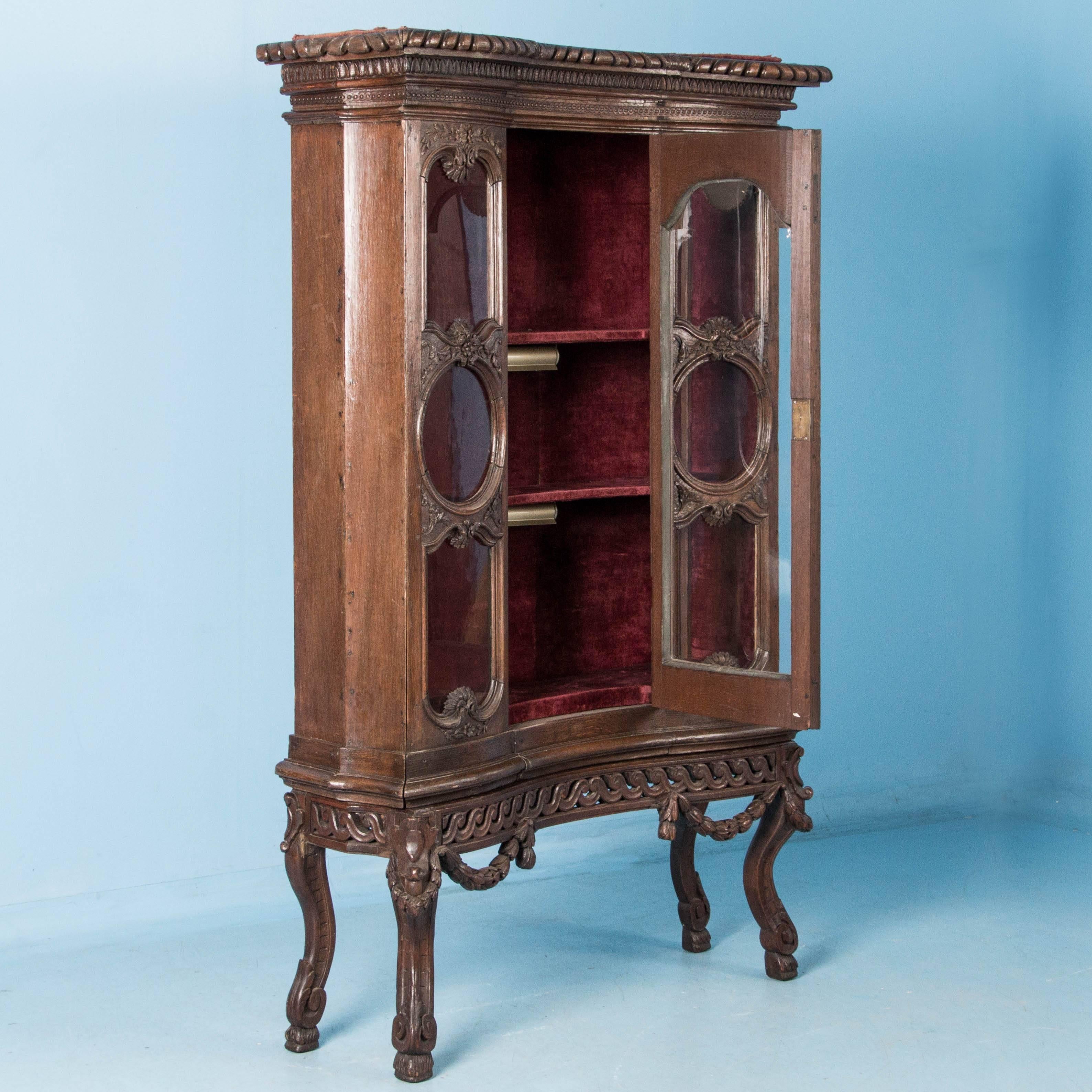 Oak china cabinet made in two parts, with a single concave glass door flanked by three glass panels. Each of the three panels and door on the upper cabinet are accented by carved molding. The case rests on a heavily carved base with four curved and