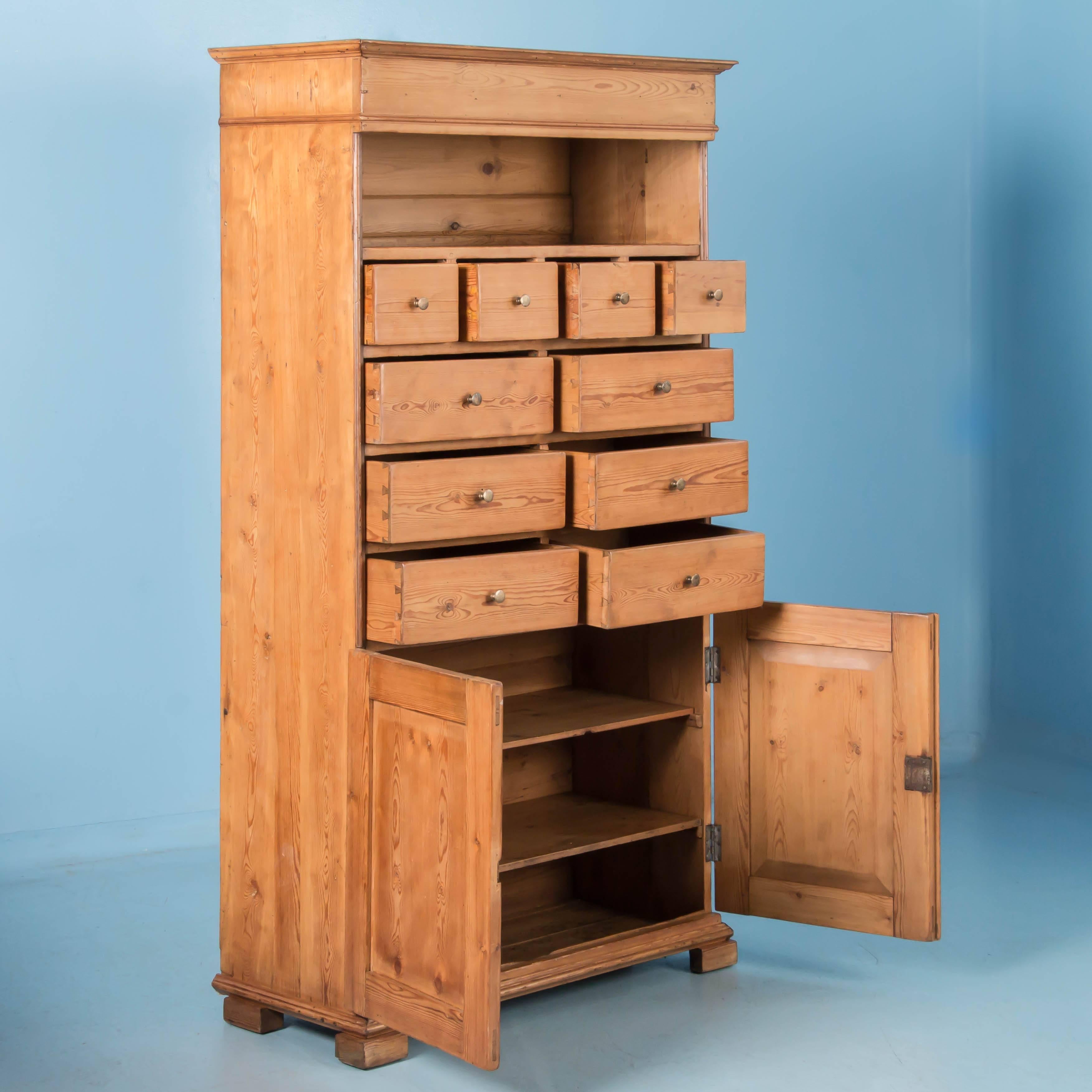 Tall antique pine cabinet from Denmark with an assortment of storage options, from the open space above to the drawers in the middle and cupboard doors below. There are a total of ten drawers, four small drawers above six half drawers. Notice how