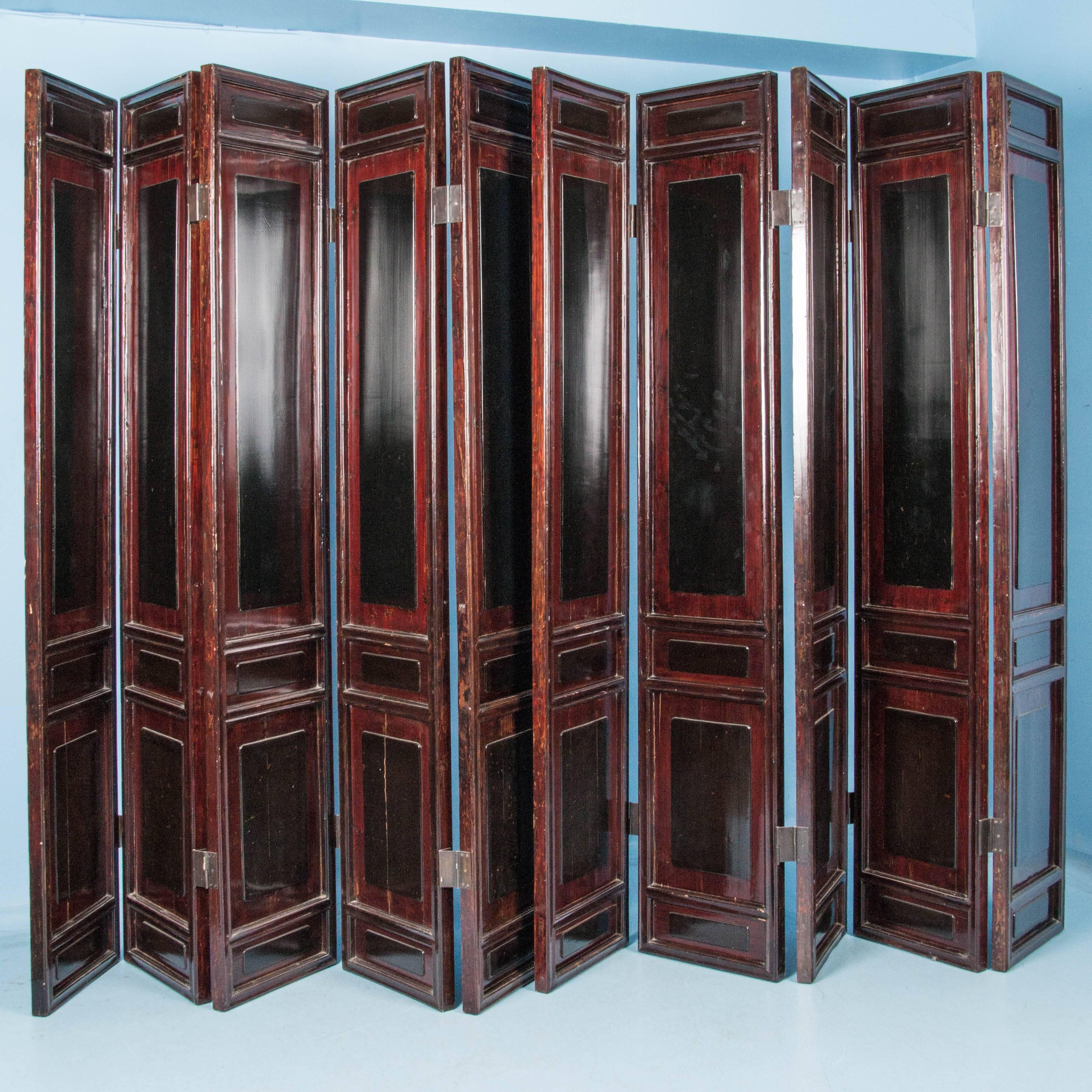 Grand set of ten red lacquered panels with brass hinges and accents of black on each of the raised panels. The color and design are the same on both sides. We have separated the screen into two freestanding screens with five hinged panels each (the