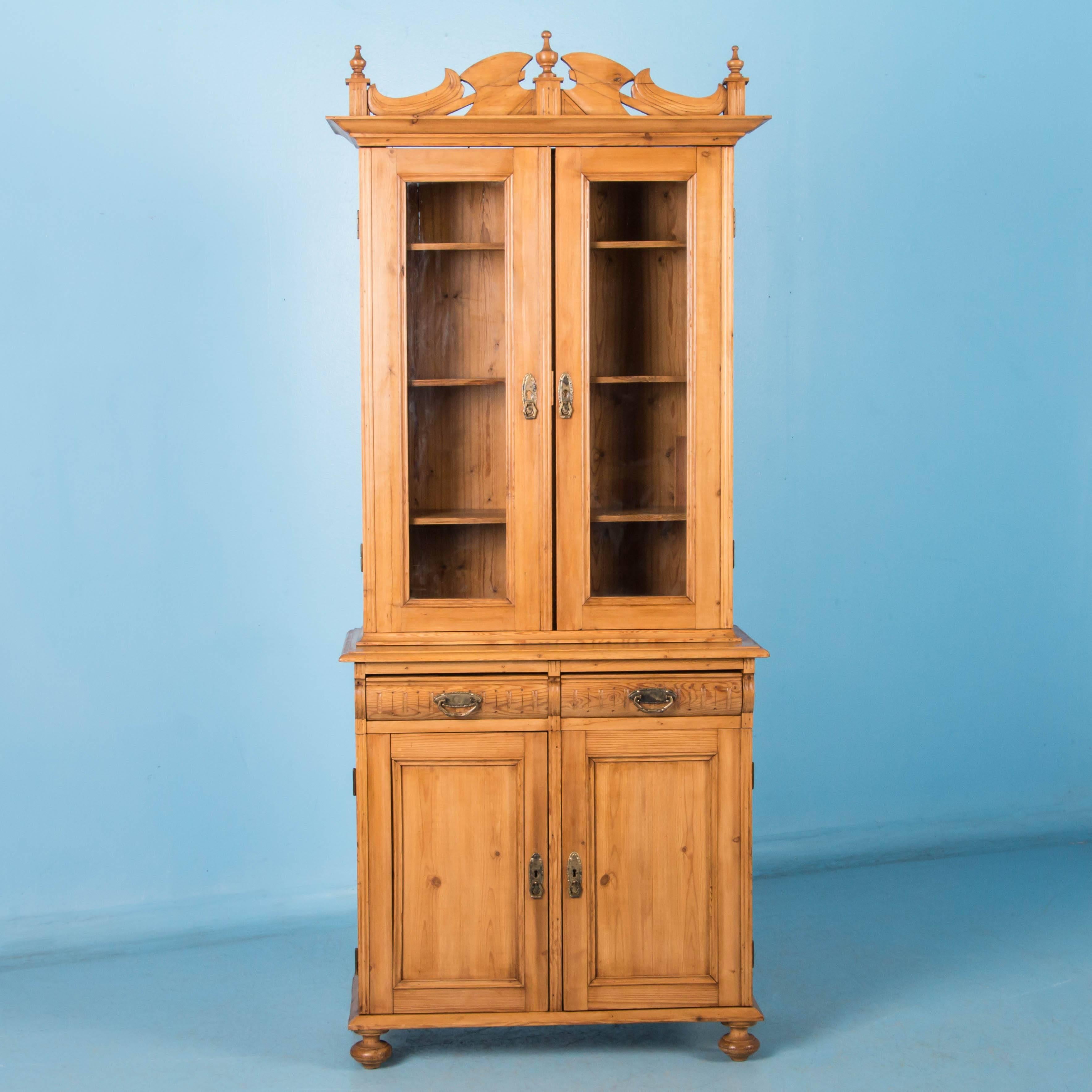 This tall, narrow cabinet is made in two sections with adjustable shelving behind the two glazed doors above, and two drawers with cupboard space below. The natural pine bookcase has been sealed with a satin wax finish.