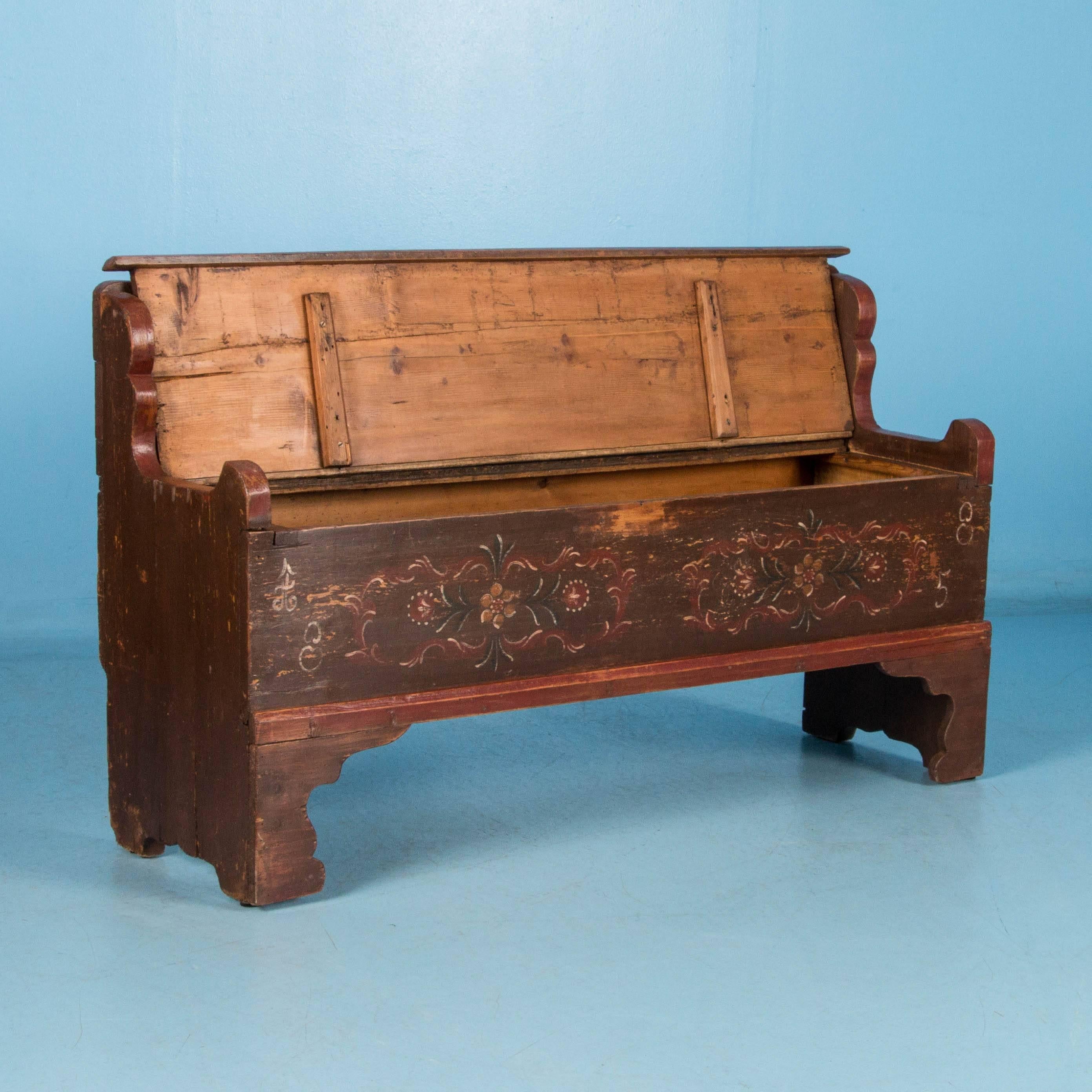 This antique storage bench features the original polychrome Folk Art paint on a rust colored background with the date 1885. The hinged seat lifts up to access the large storage space within. Please take a moment to enlarge the photos and examine the