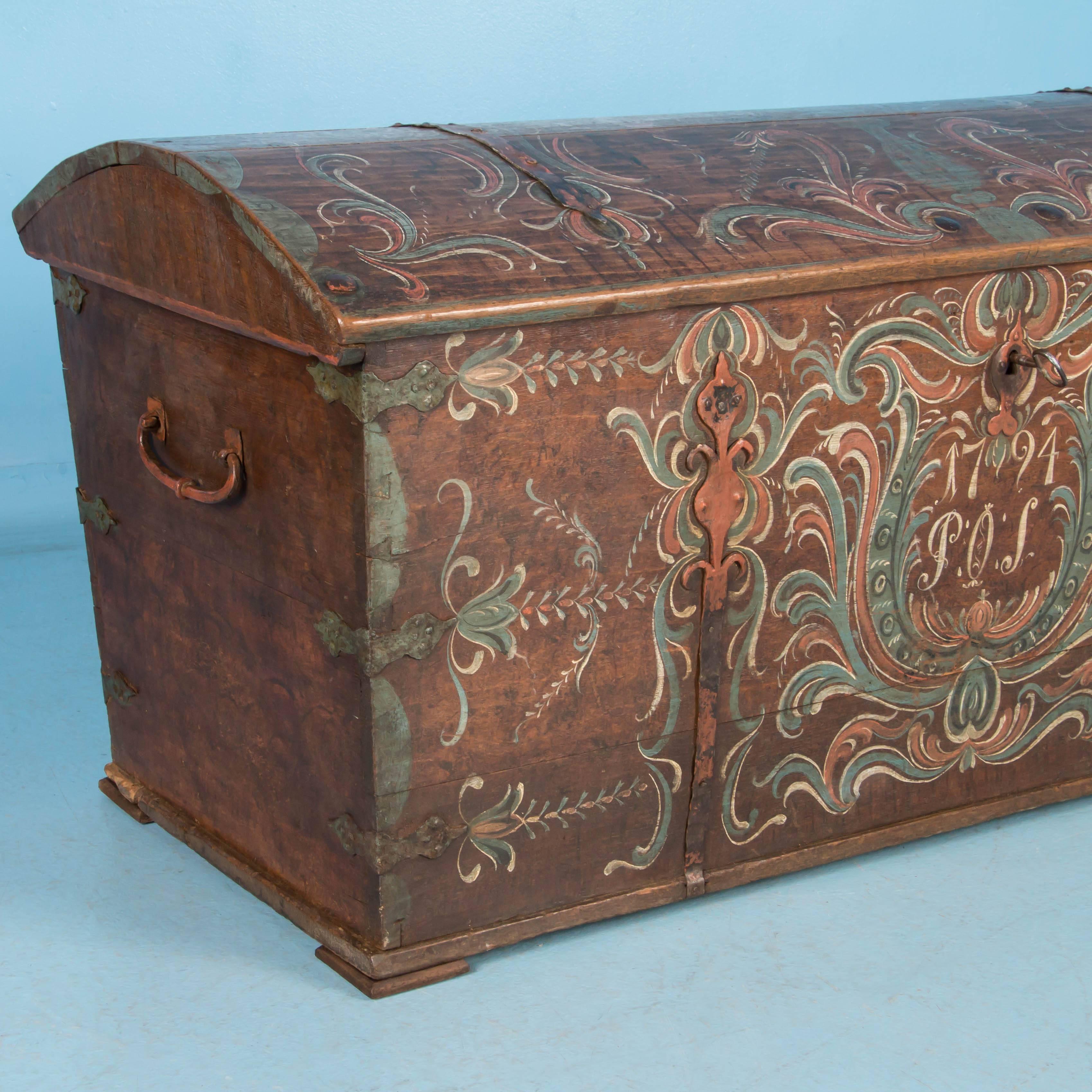 Made of solid oak boards, this trunk from Sweden is painted in a green, white and rust Folk Art design on a brown background with the date 1794 and the initials P.O.S. painted on the front. There is a slight separation of the boards on the dome top