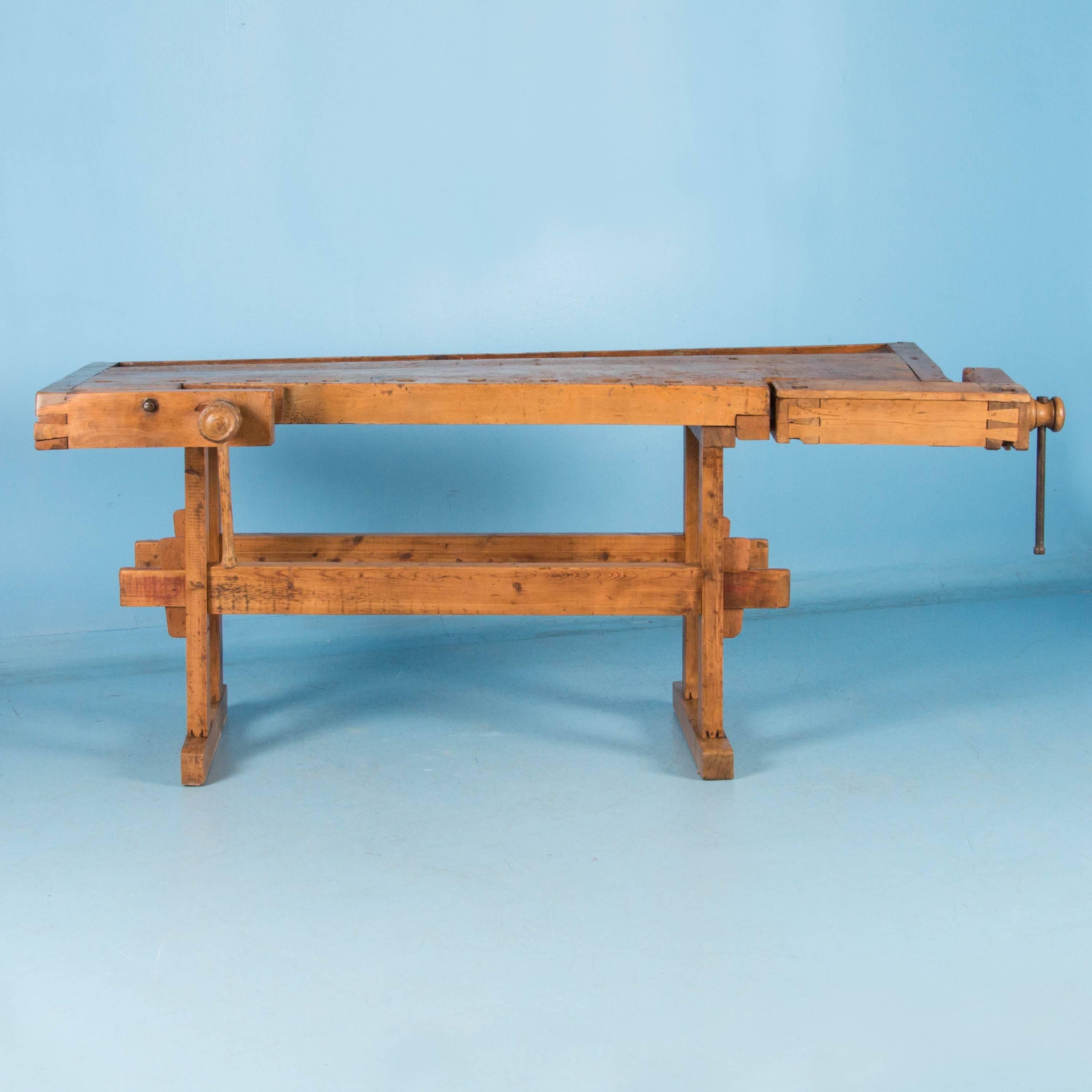 This circa 1900 antique workbench is made of a variety of hardwoods. It has a pair of working wood handled vices and a recessed tray where the carpenter would lay his tools and for catching debris. The bench top is flat but not level, with a twist