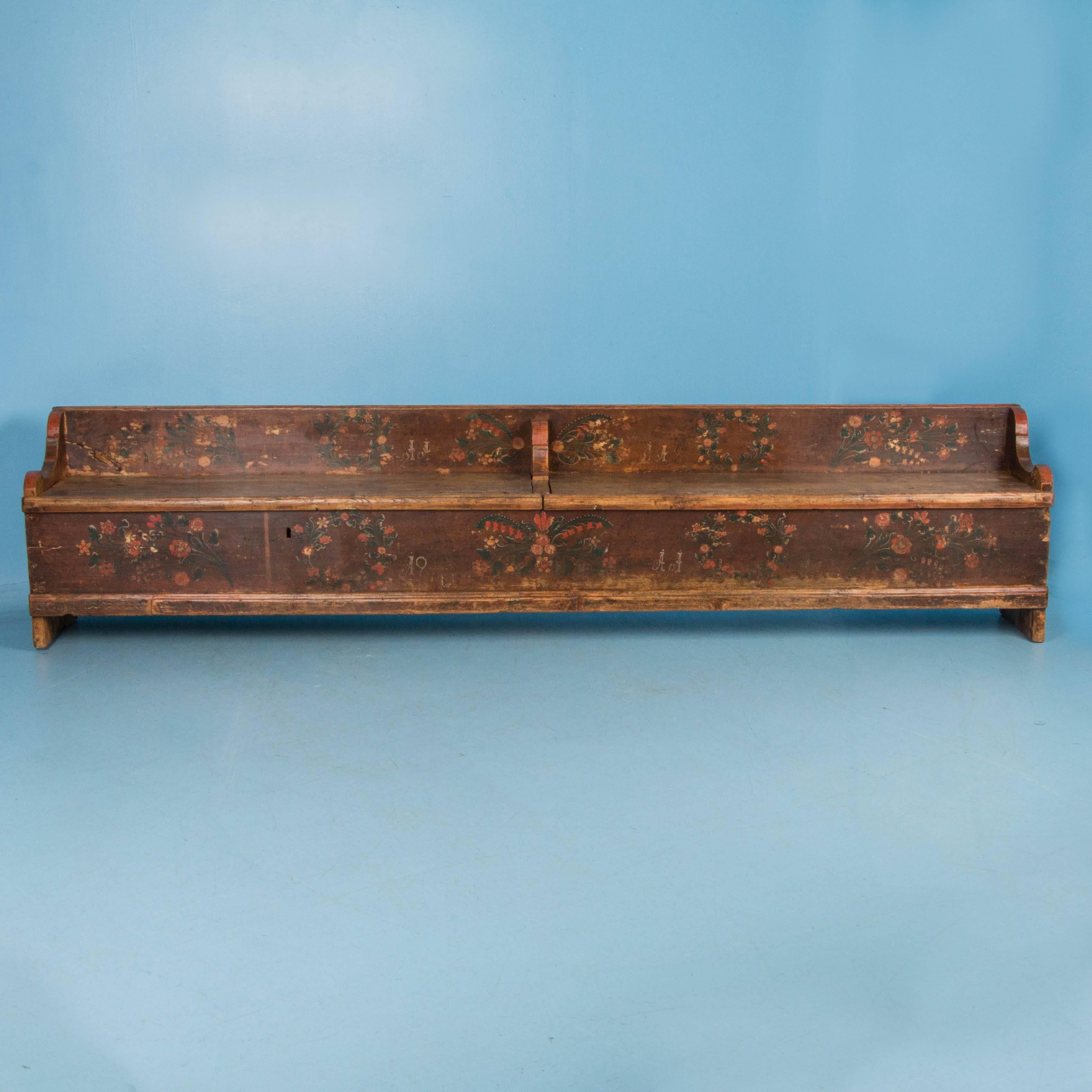 This long antique storage bench from Romania is made of pine and painted with traditional polychrome floral designs over a rich brown base color. Underneath the segregated hinged seats are two large storage compartments. The original painted finish