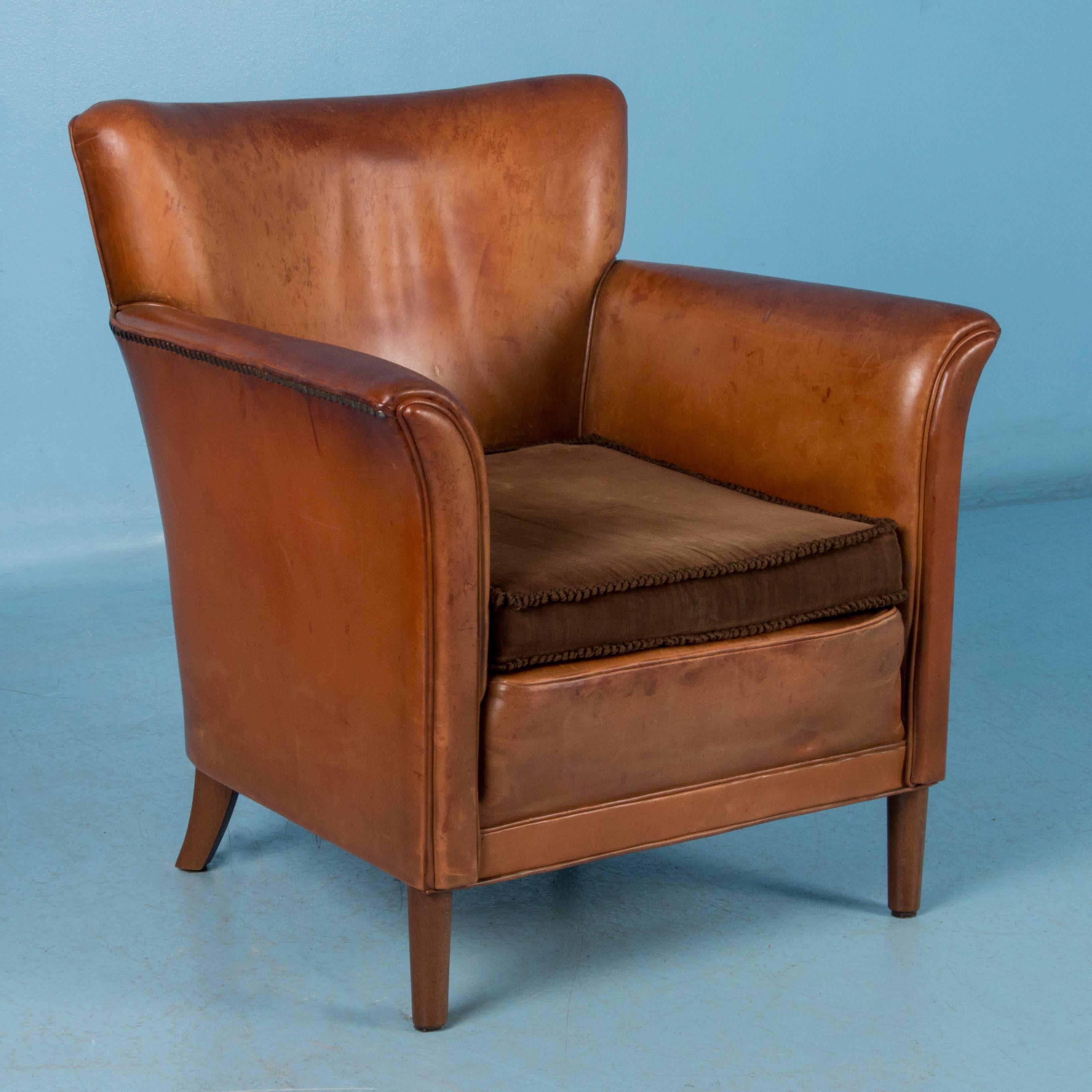 This pair of early 20th century leather club chairs from Denmark have a square removable cushion and both are upholstered with decorative brass tacks. The wing backs of both chairs create a slight curve for more comfort and the arms are slightly
