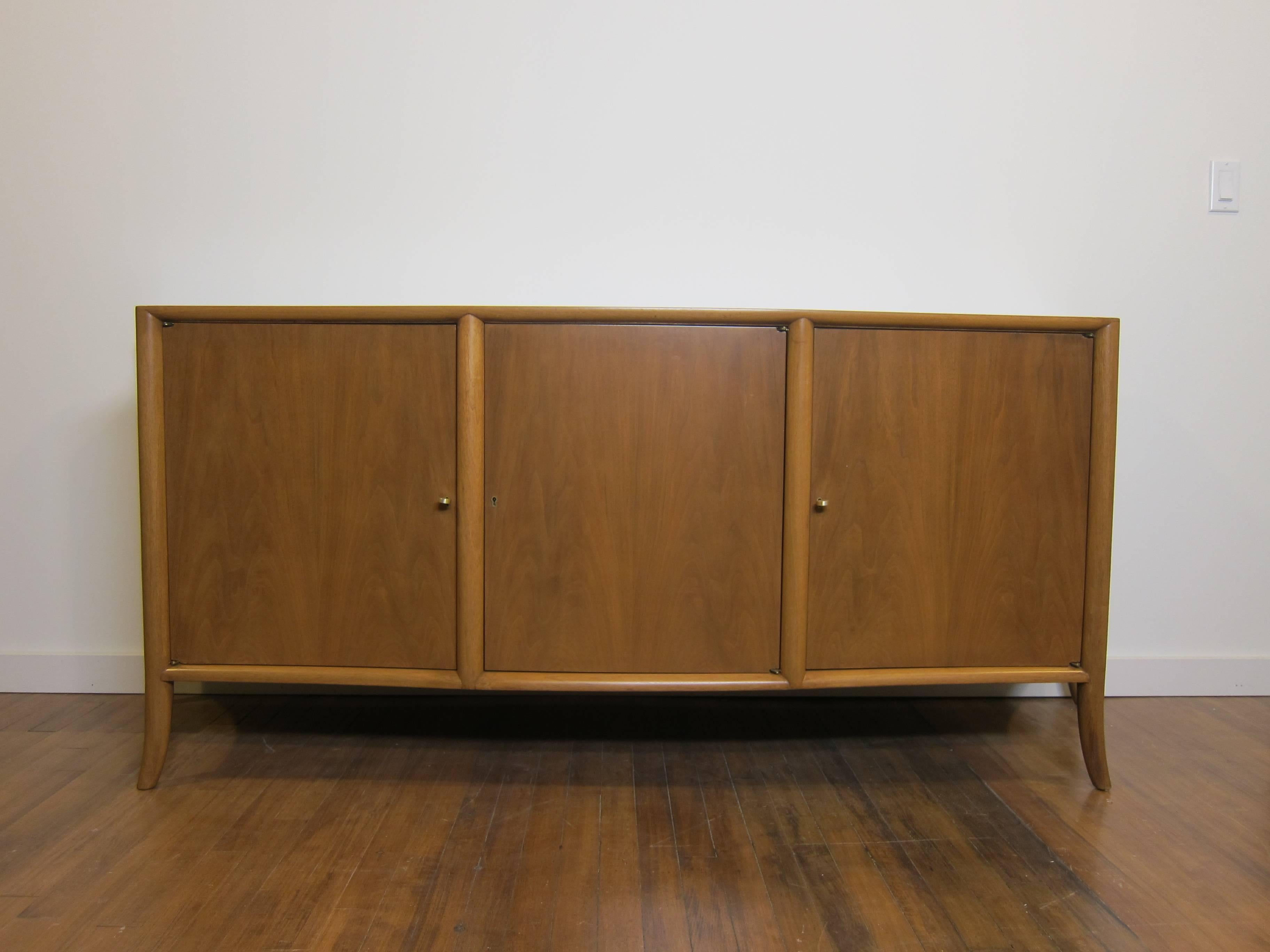 An elegant Saber leg sideboard designed by T.H. Robsjohn-Gibbings for Widdicomb.  T.H. Robsjohn Gibbings Credenza mid century.  Bleached mahogany with bowed front and tapered sides. Inside four drawers with shelving, maintains two original keys.