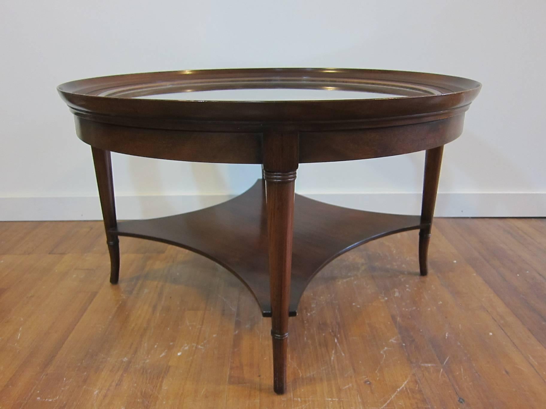 1950, saber leg round glass top cocktail table in walnut by Kittinger. Elegant cocktail table with neoclassical style in very good condition. Glass has scratches consistent with age and use. For an additional $225.00 we will replace with new
