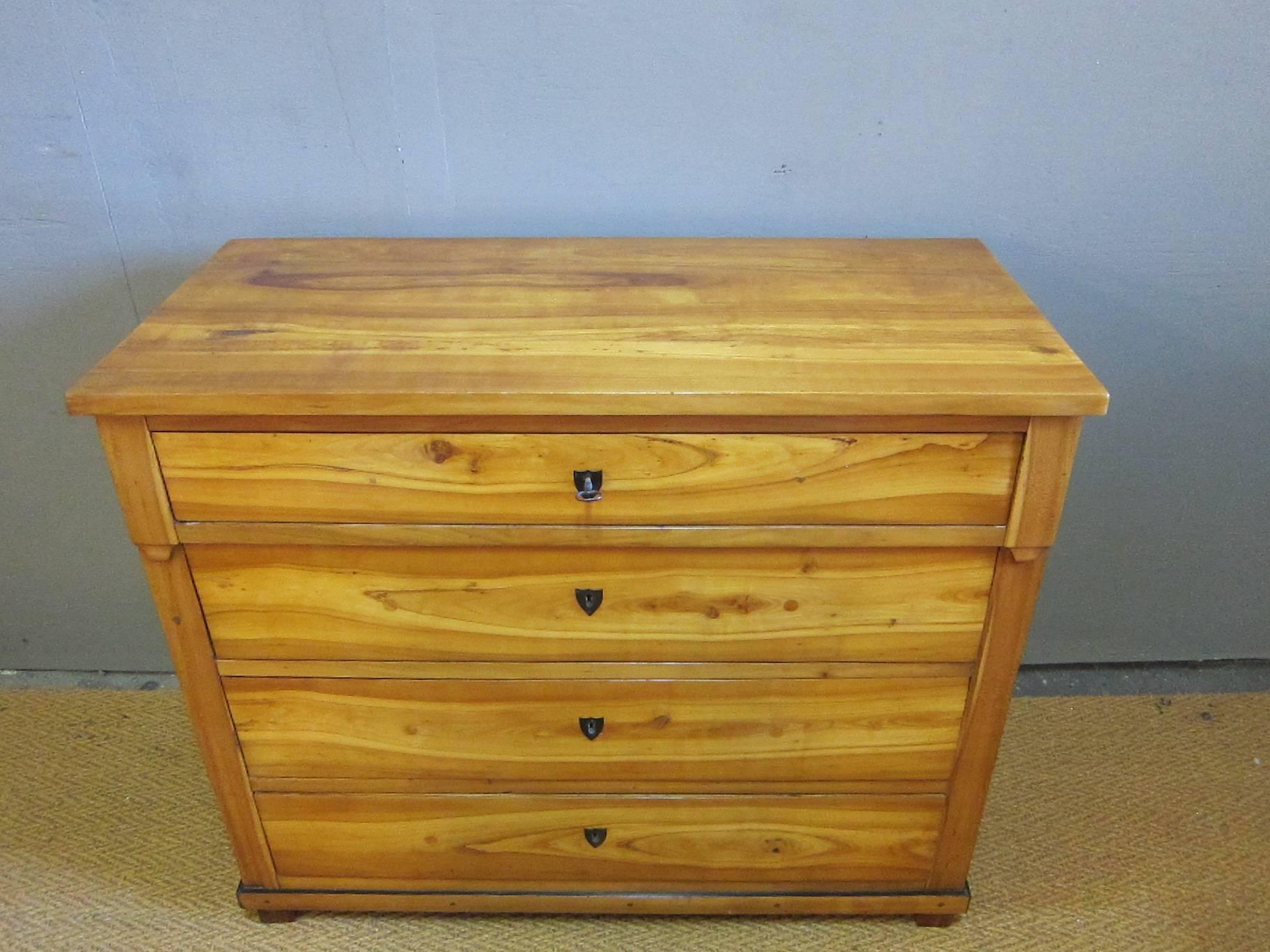 Period Biedermeier chest of drawers. Having four drawers, simple over hang detail to top frame on block feet. Cherry veneer over northern pine (pinotea), drawer fronts having buffalo horn escutcheons with working locks. Drawers exhibit plugged holes