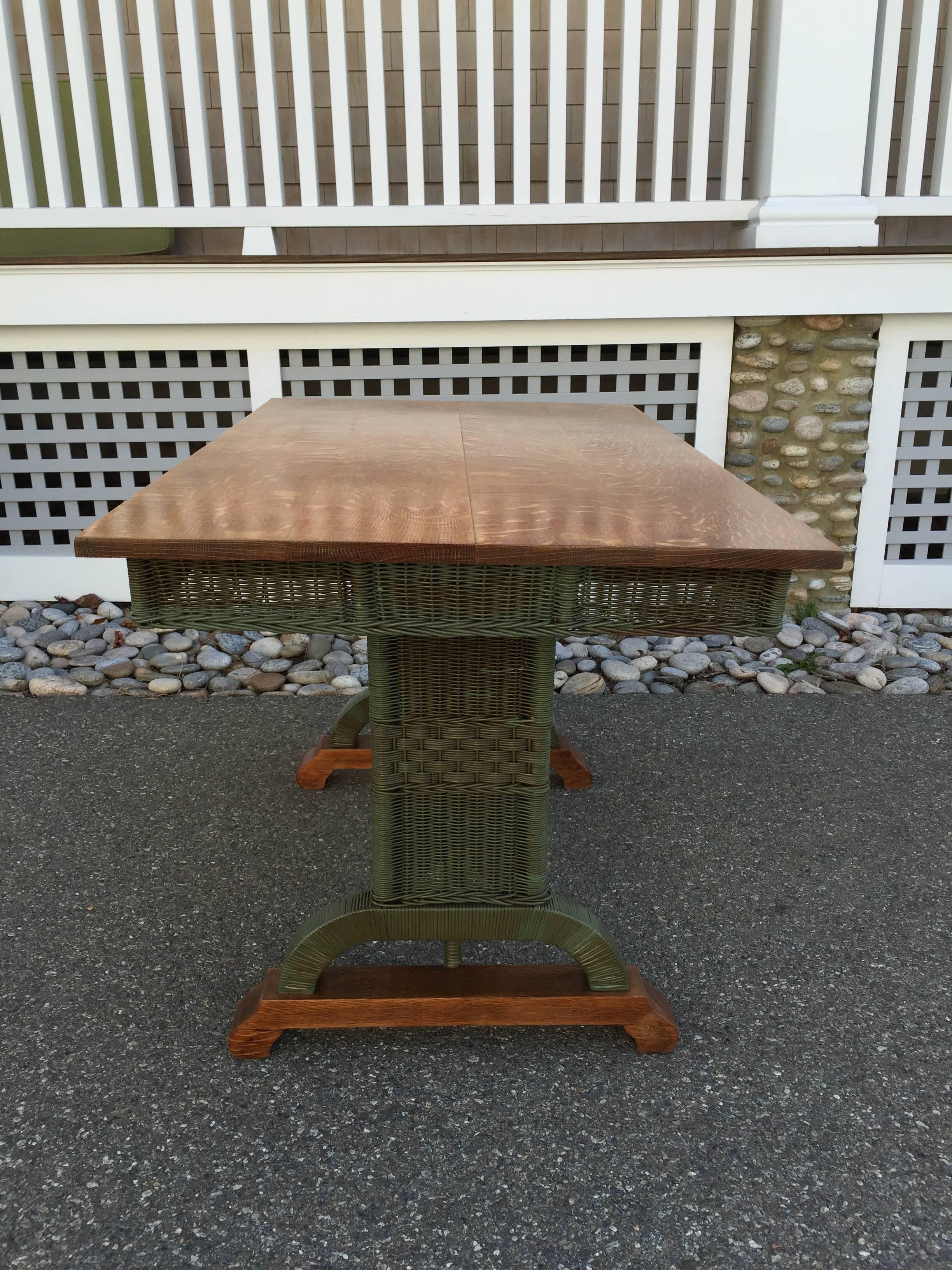 Beautiful antique wicker library table in faded green paint with quarter sawn oak top and base. Table measures 50" long, 30" wide and 30" tall. Slight separation of planks in oak top.